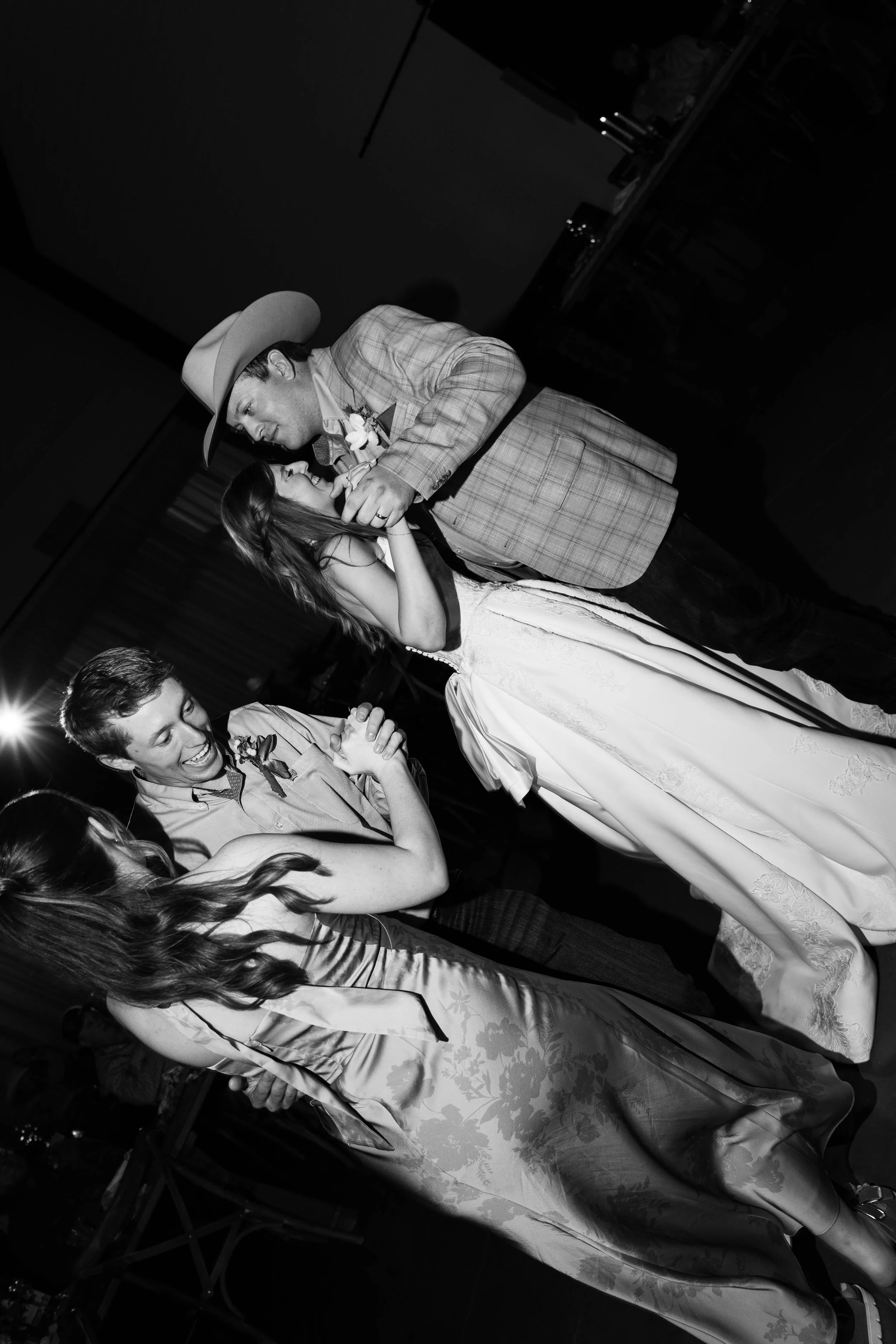 A young couple dancing closely at a celebration or wedding reception, surrounded by other party guests.