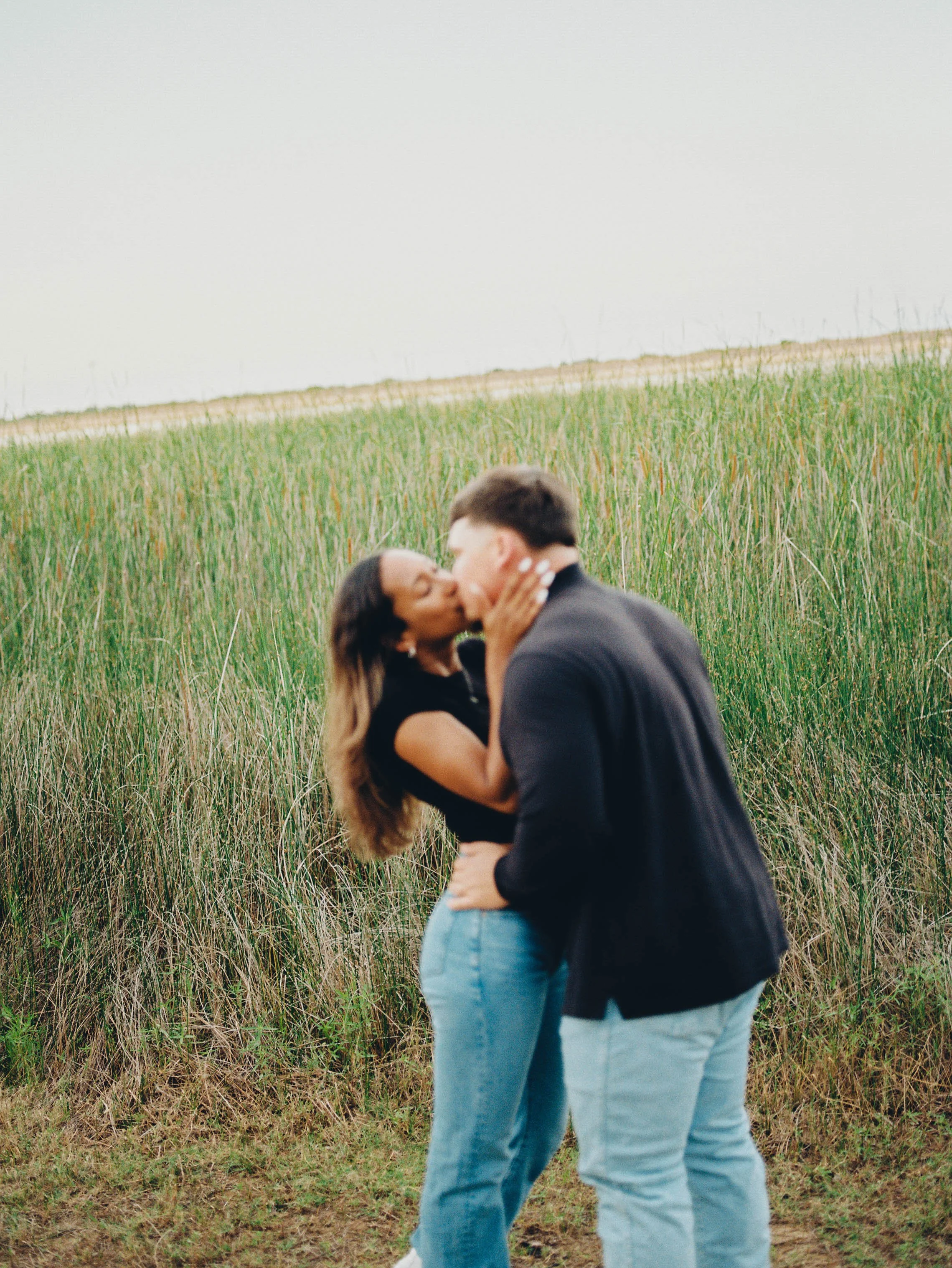 A couple kissing outdoors in a field of tall grass