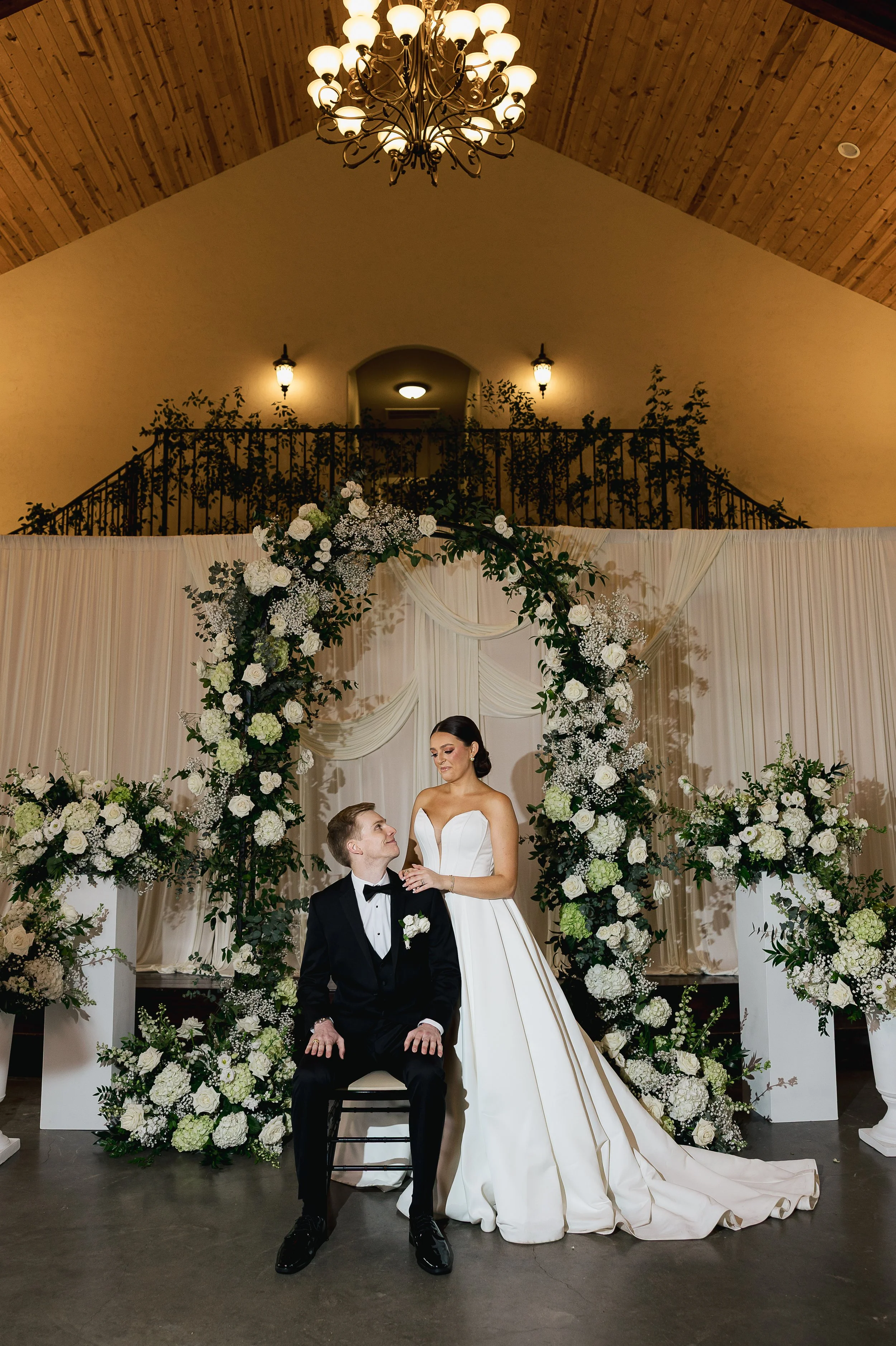 Bride and groom at their wedding ceremony with floral arch and draped backdrop.