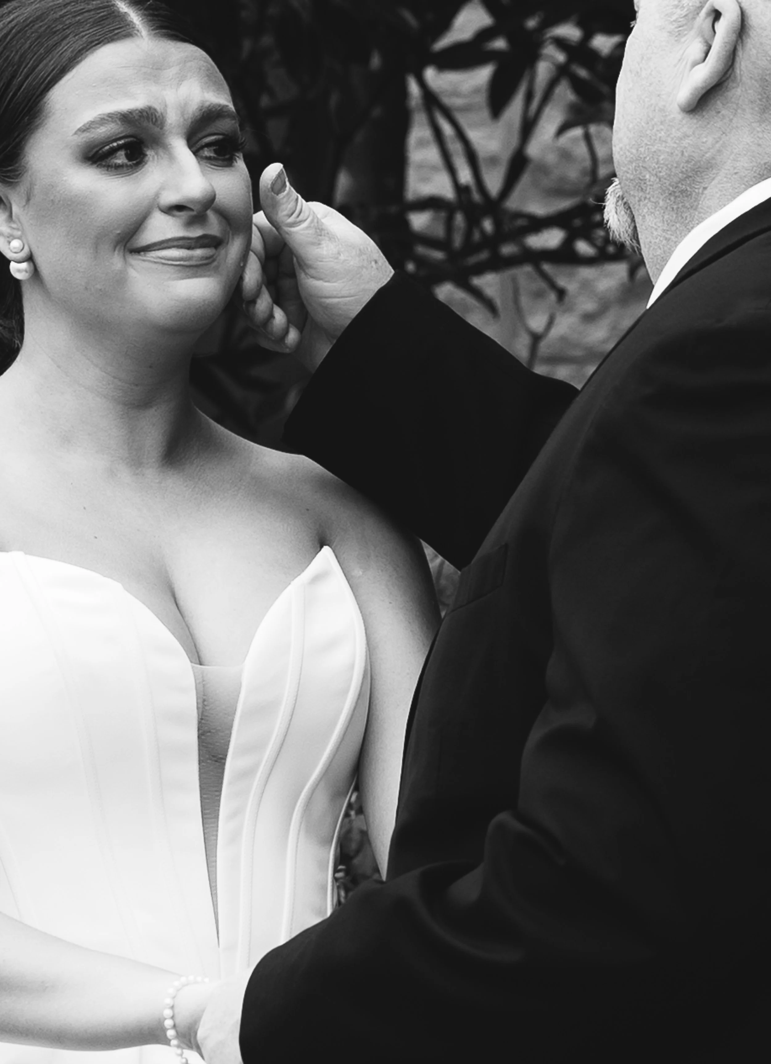 A black and white photo of a bride and groom during their wedding ceremony. The groom is holding the bride's chin as she looks at him emotionally.