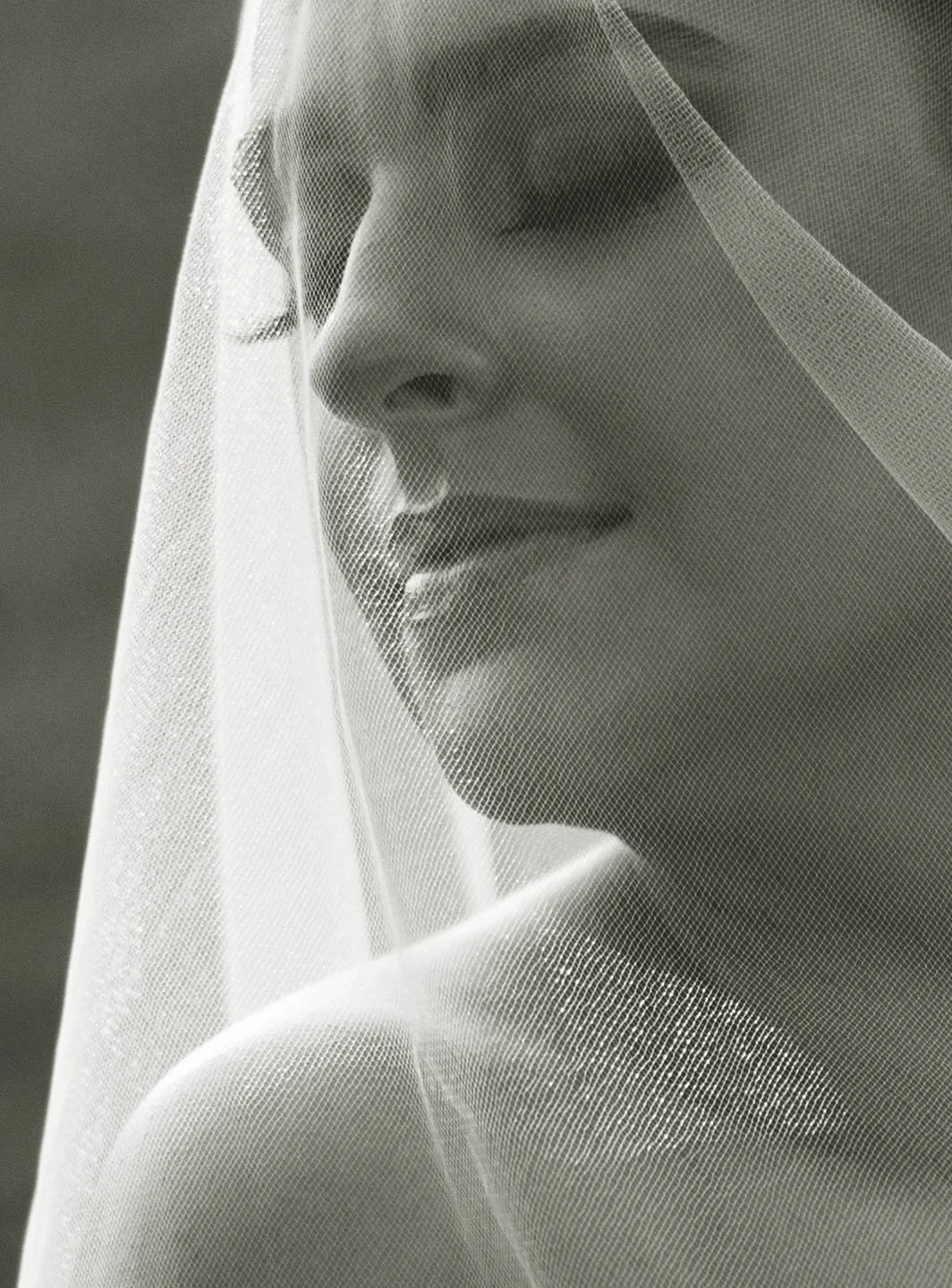A close-up black-and-white photograph of a woman with closed eyes, her face partly covered by a translucent veil.