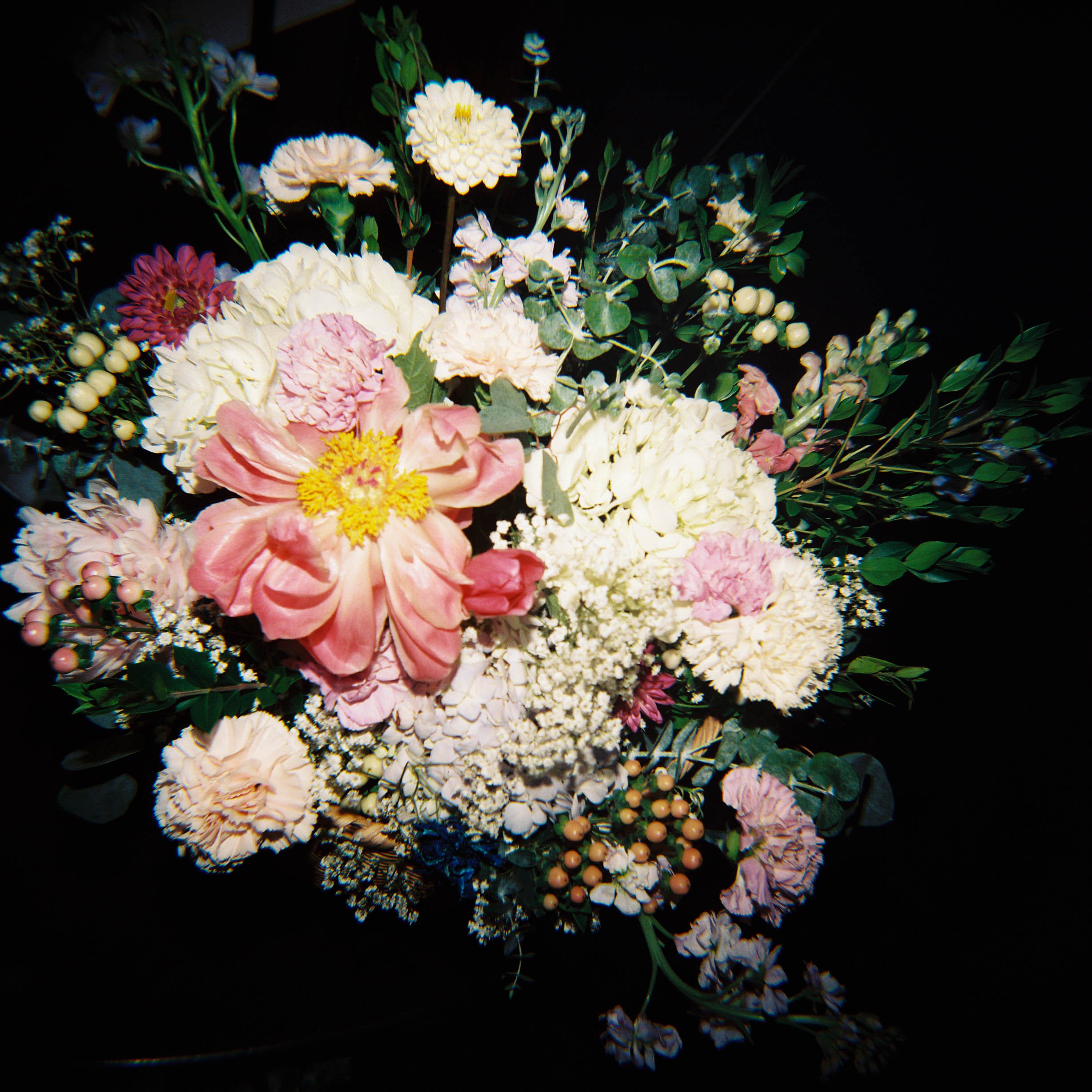 A bouquet of various flowers including pink, white, and purple blossoms with green leaves and small white berries, set against a black background.