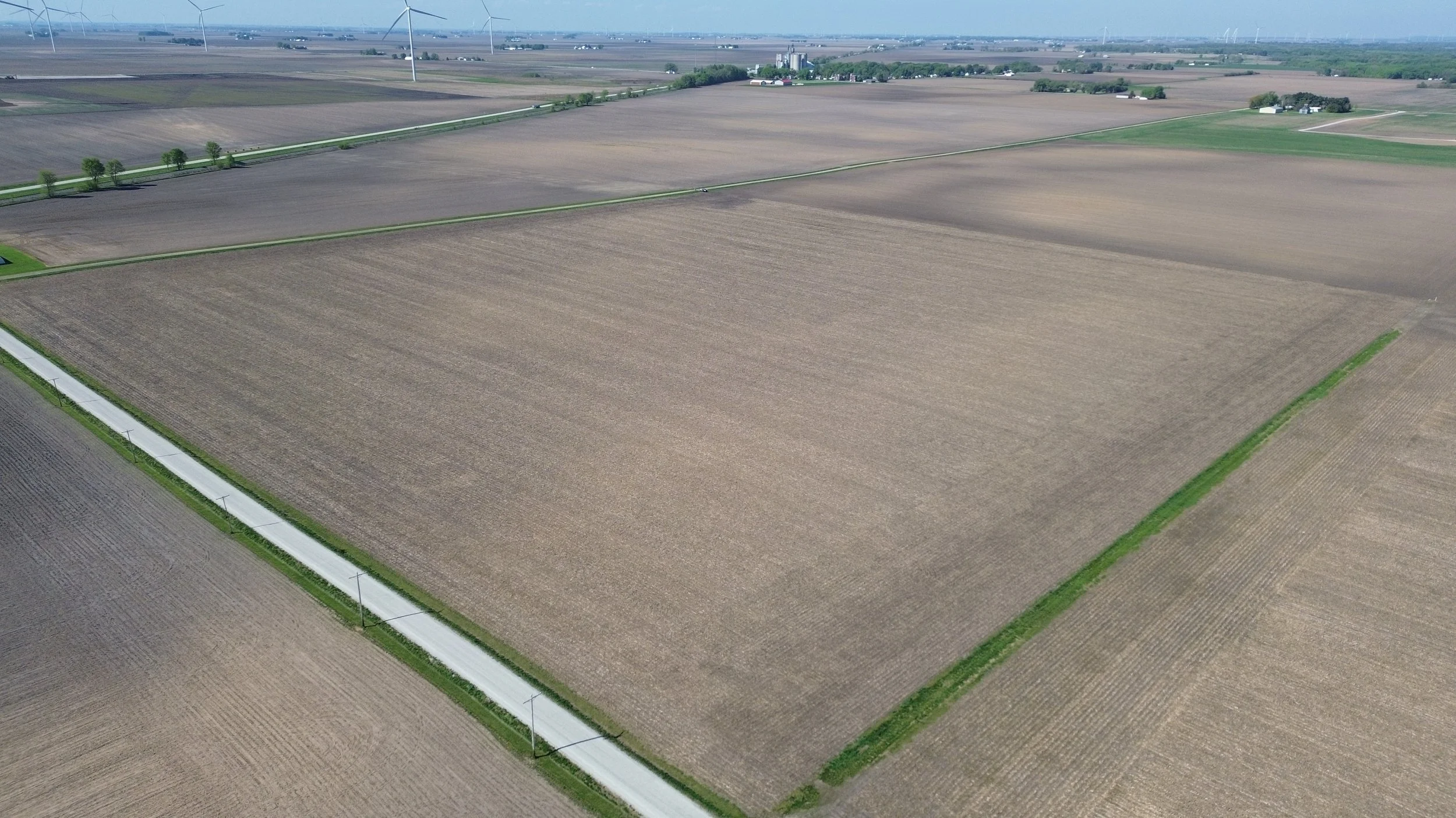 Aerial view of rolling green farmland and fields with scattered trees under a partly cloudy sky.