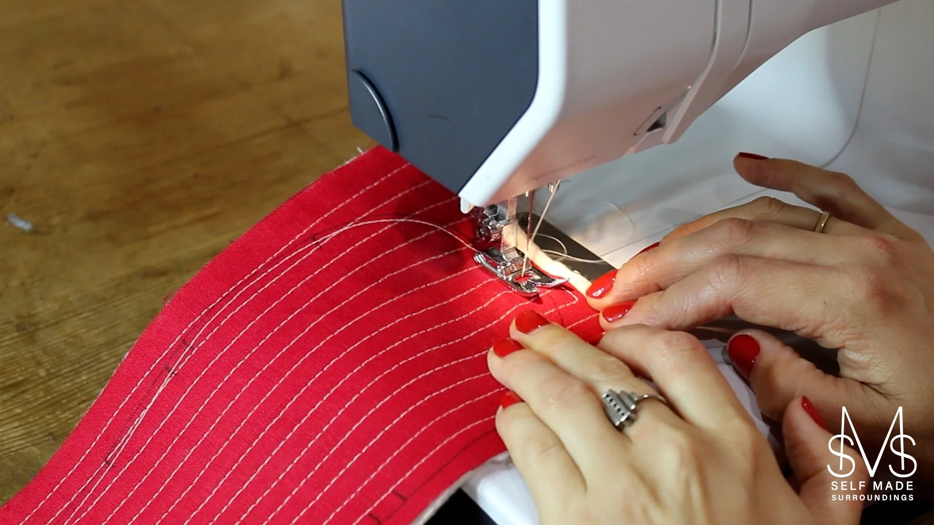 A person machine basting a layer of quilted fabric and felt backing to form a slipper sole, using a sewing machine.