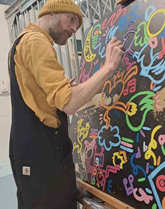Un homme dessine avec des couleurs vives sur une toile noire, créant une œuvre d'art abstraite et colorée.