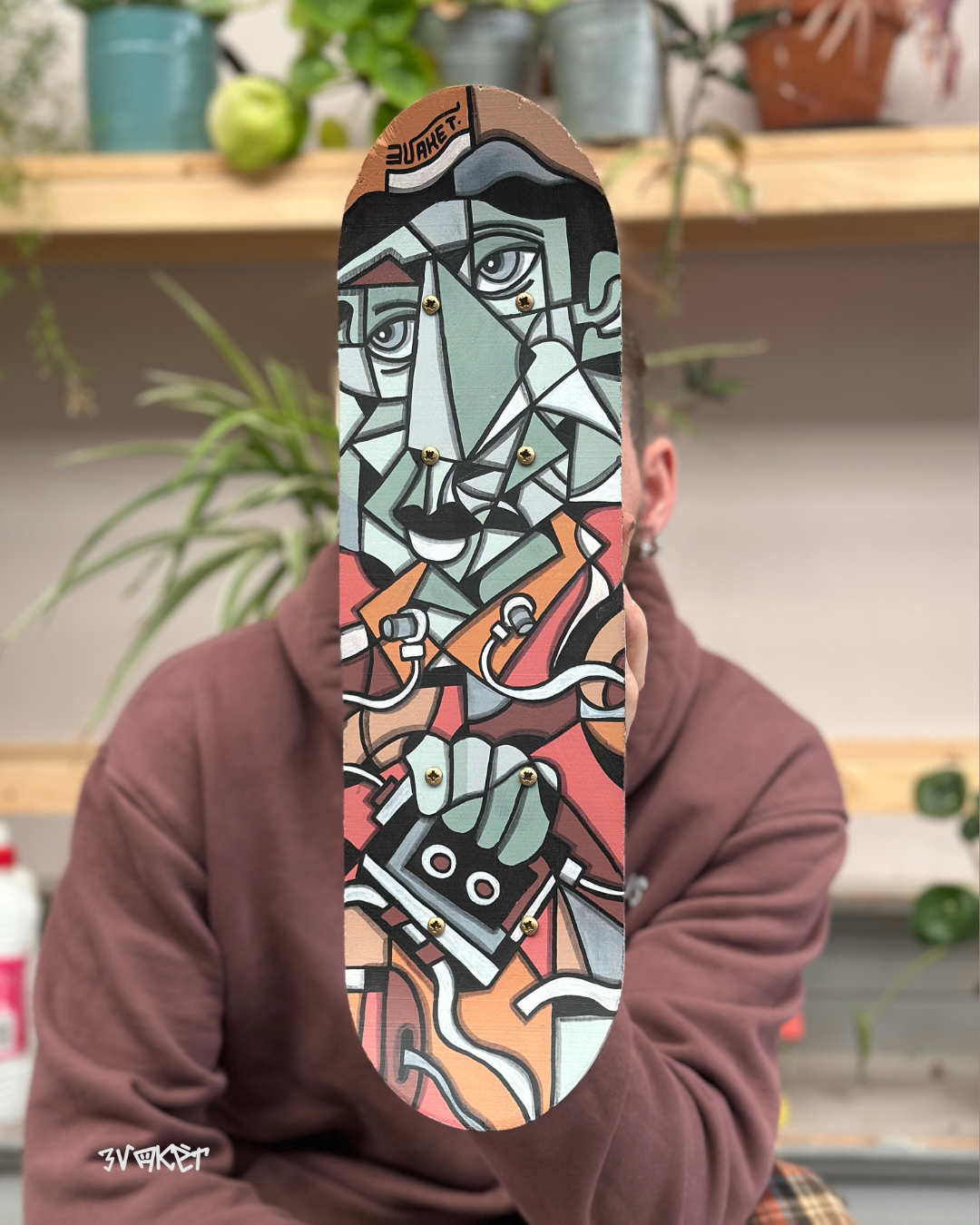 Person tenant un skateboard avec une peinture abstraite représentant un visage.