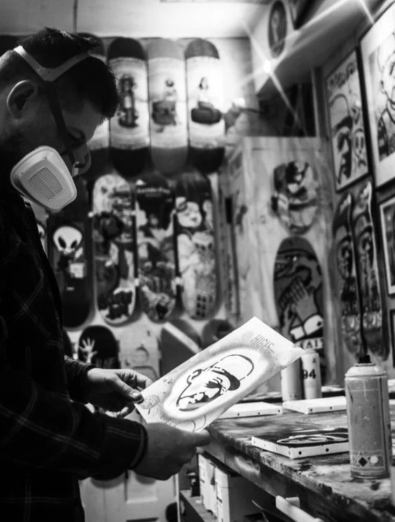 Un artiste regarde un dessin avec le visage de Che Guevara dans un atelier de skateboard et d'art, avec des planches de skateboard décorées accrochées au mur en arrière-plan.