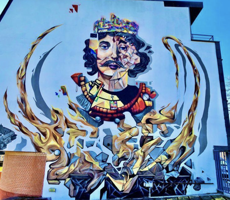 Graffiti mural représentant un visage d'homme avec un chapeau, des éléments colorés et abstraits, entouré de flammes stylisées.
