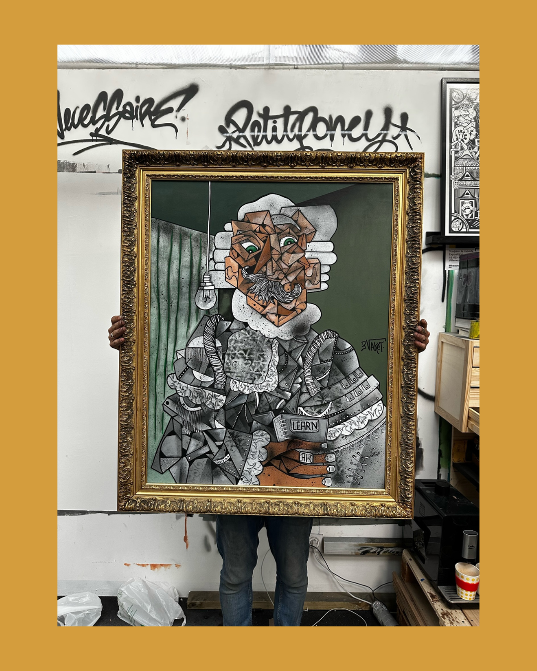 Personne tenant une grande peinture de style cubiste représentant un portrait d'homme avec un manteau et un livre intitulé 'Learn Art', dans un atelier avec graffitis sur le mur.