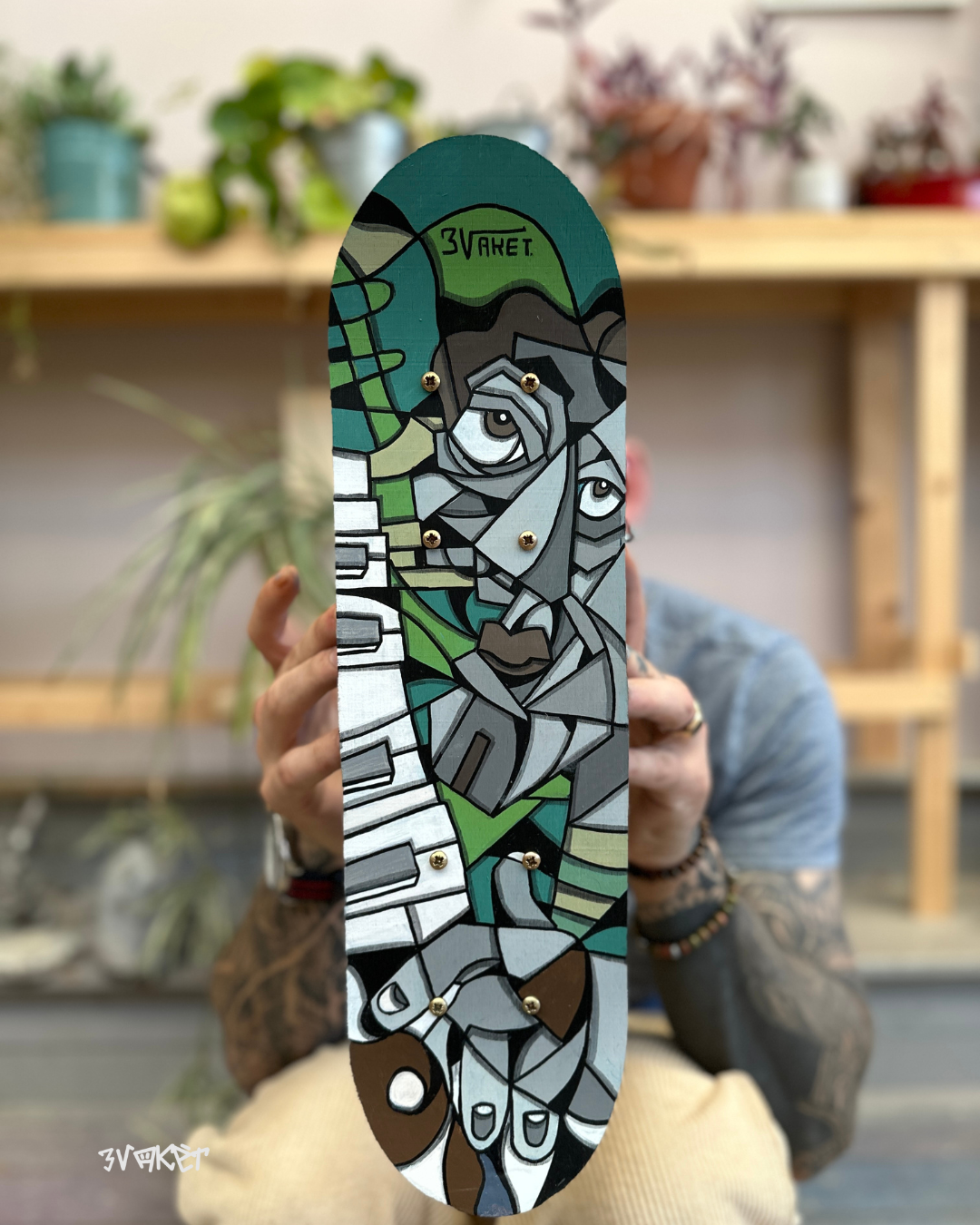 Un skate avec une peinture représentant une œuvre d'art abstraite dans un style cubiste avec des couleurs vertes, grises et noires, et une inscription '3VARET' en haut.