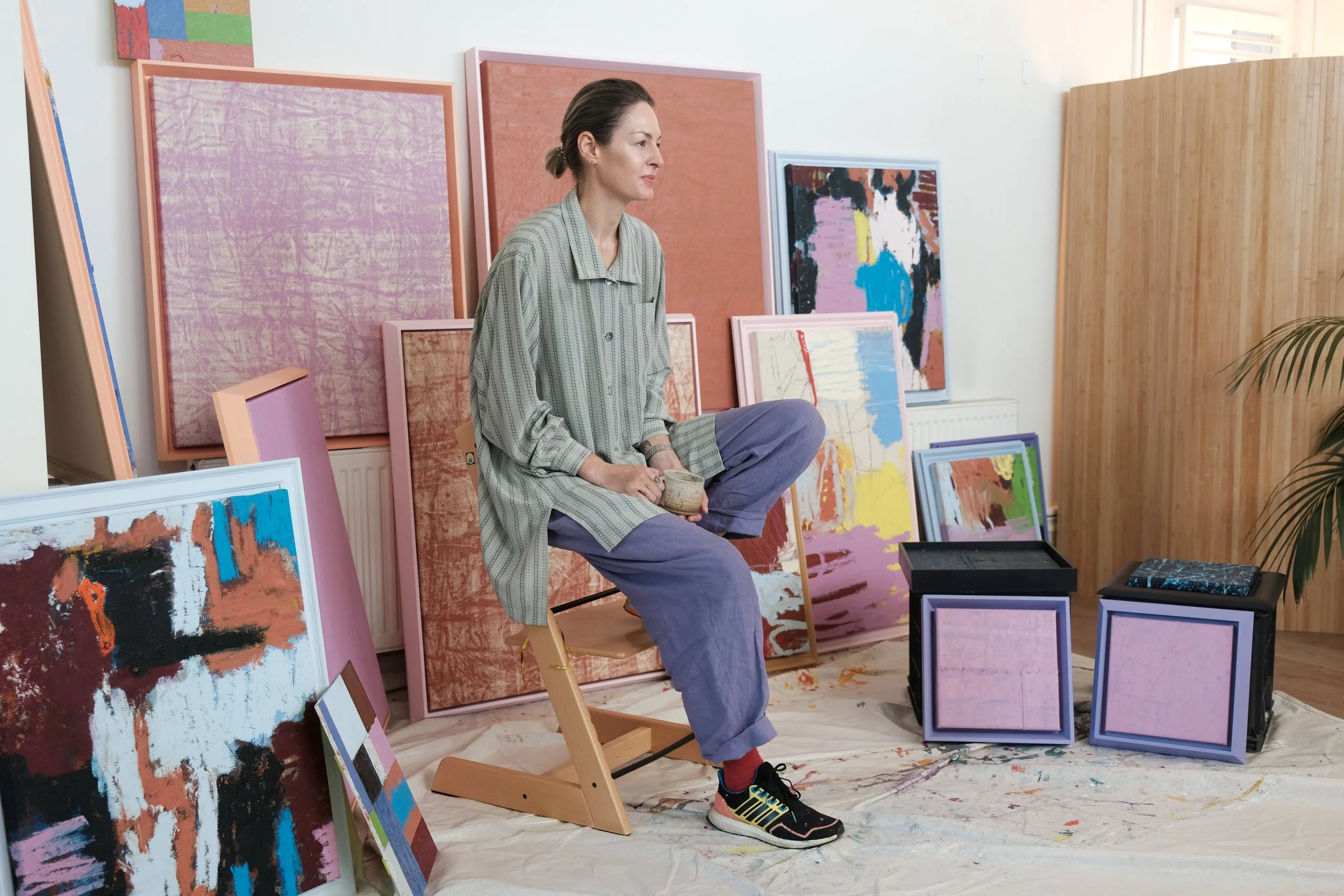 Toni Vallance sitting on a chair surrounded by her paintings