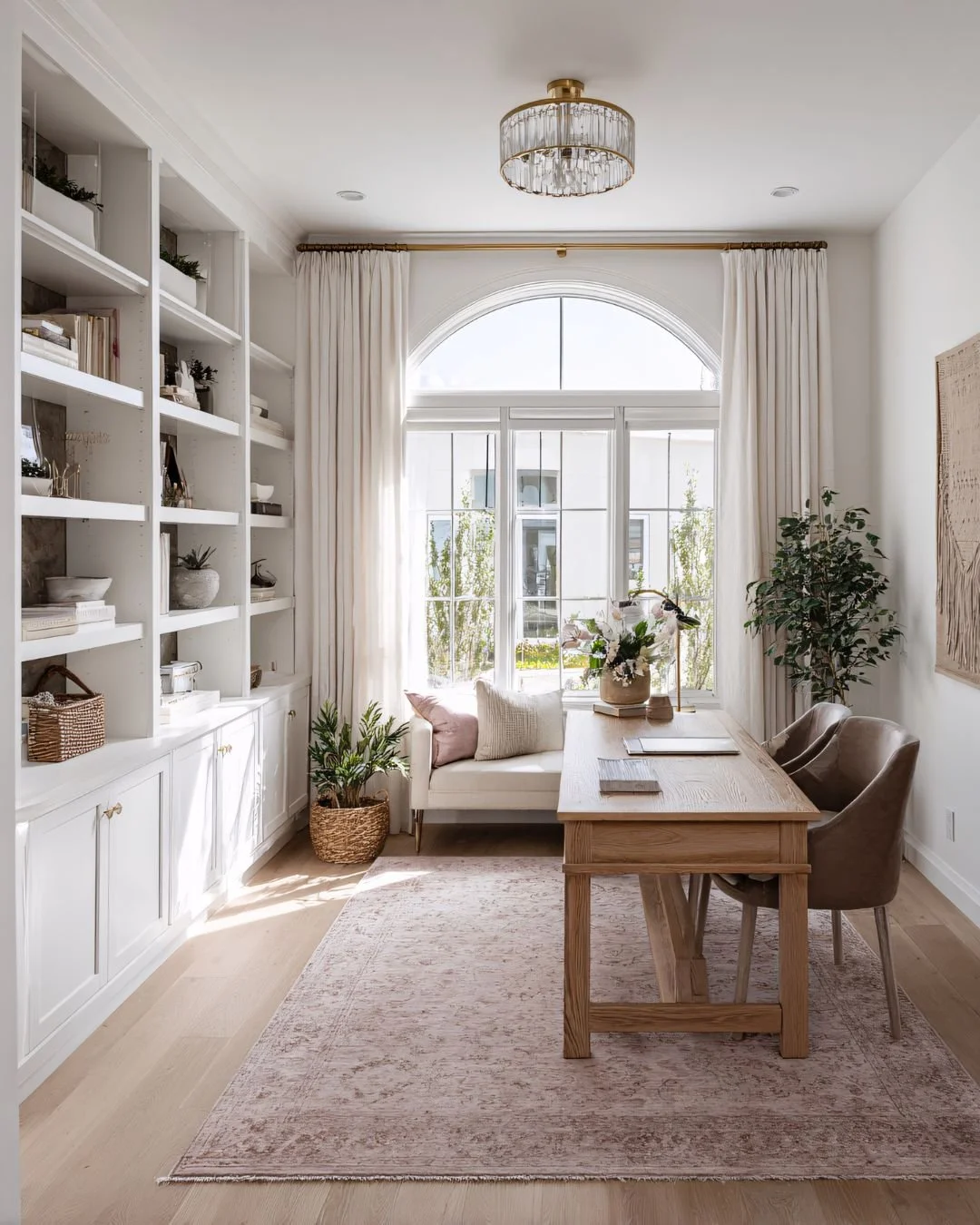 Bright reading or workspace area with a window seat, wooden desk, chairs, plants, and shelves with books.