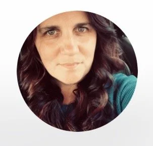 Close-up of a woman with long dark wavy hair wearing a teal top, looking at the camera with a slight smile.