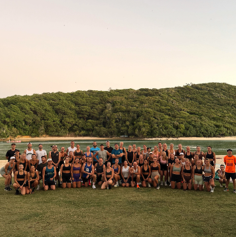 Group of people posing outdoors near water with a forested hill in the background.