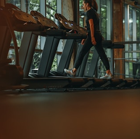 A woman in workout clothes walking on a treadmill in a gym.