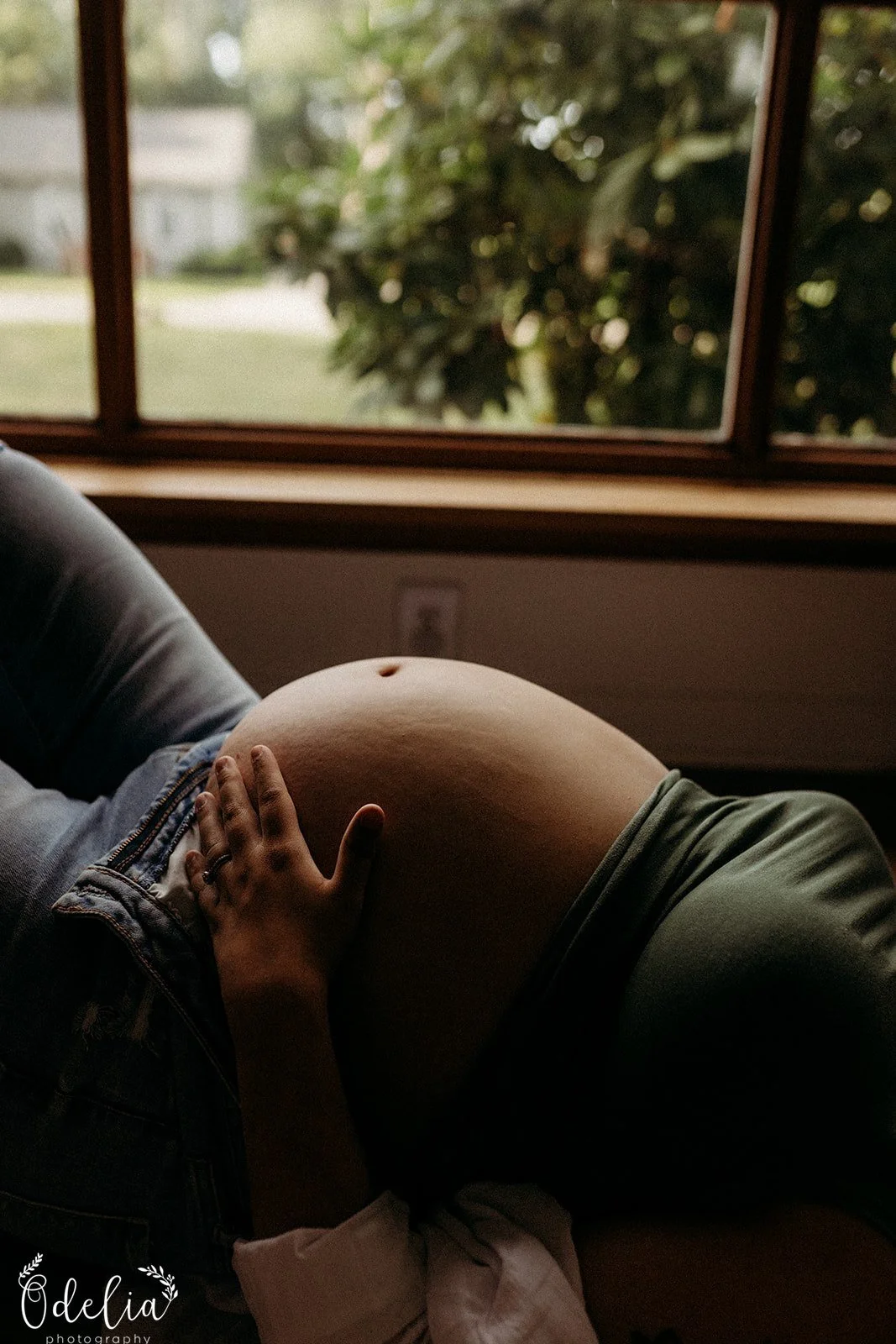 A pregnant person lying on their side near a window, with one hand resting on their belly.
