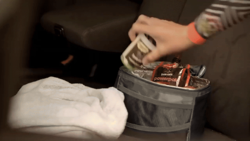Person reaching into a gray cooler bag containing energy bars, with a white towel on a surface nearby.