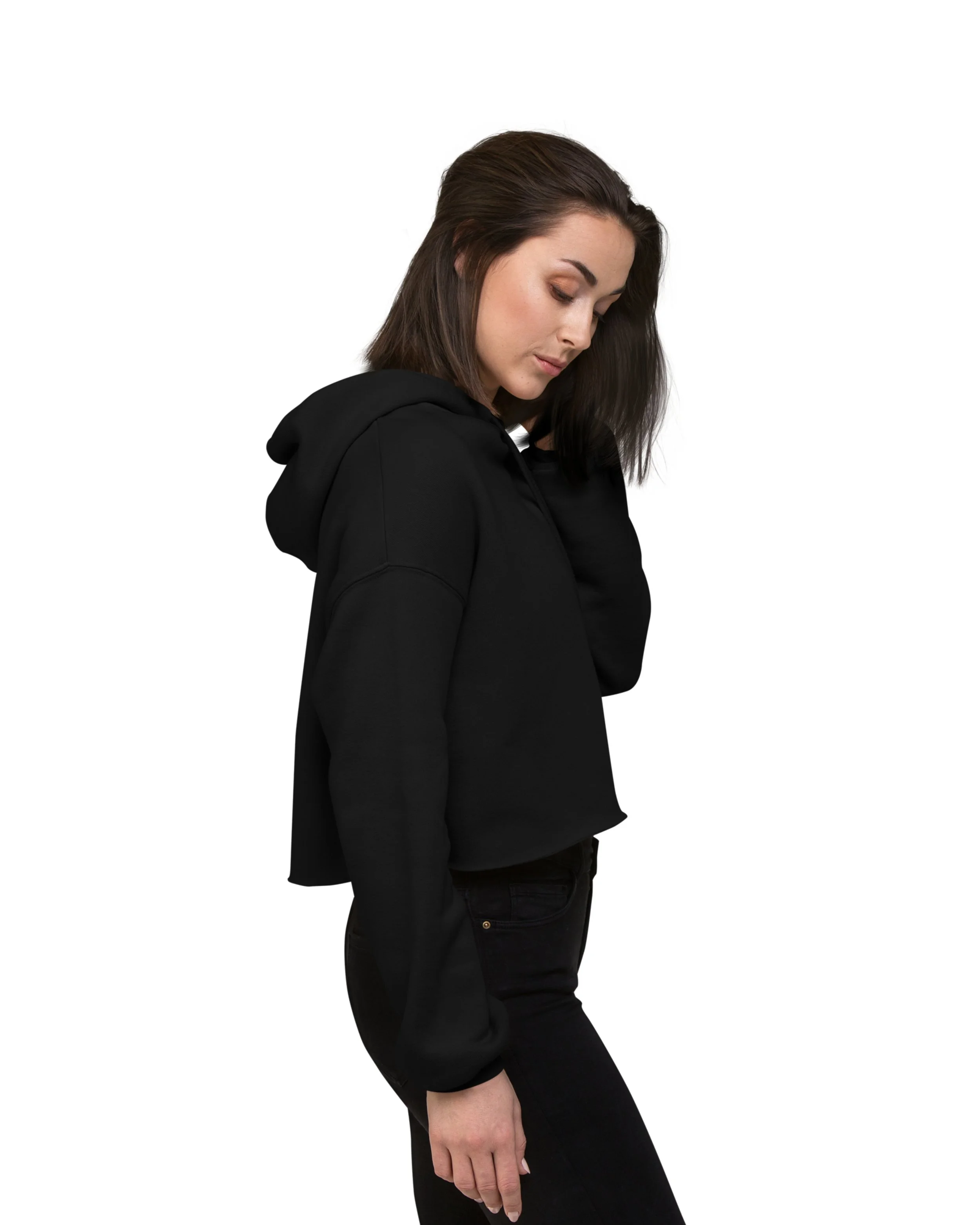 Young woman in black hoodie and black jeans looking down, side view, plain white background.