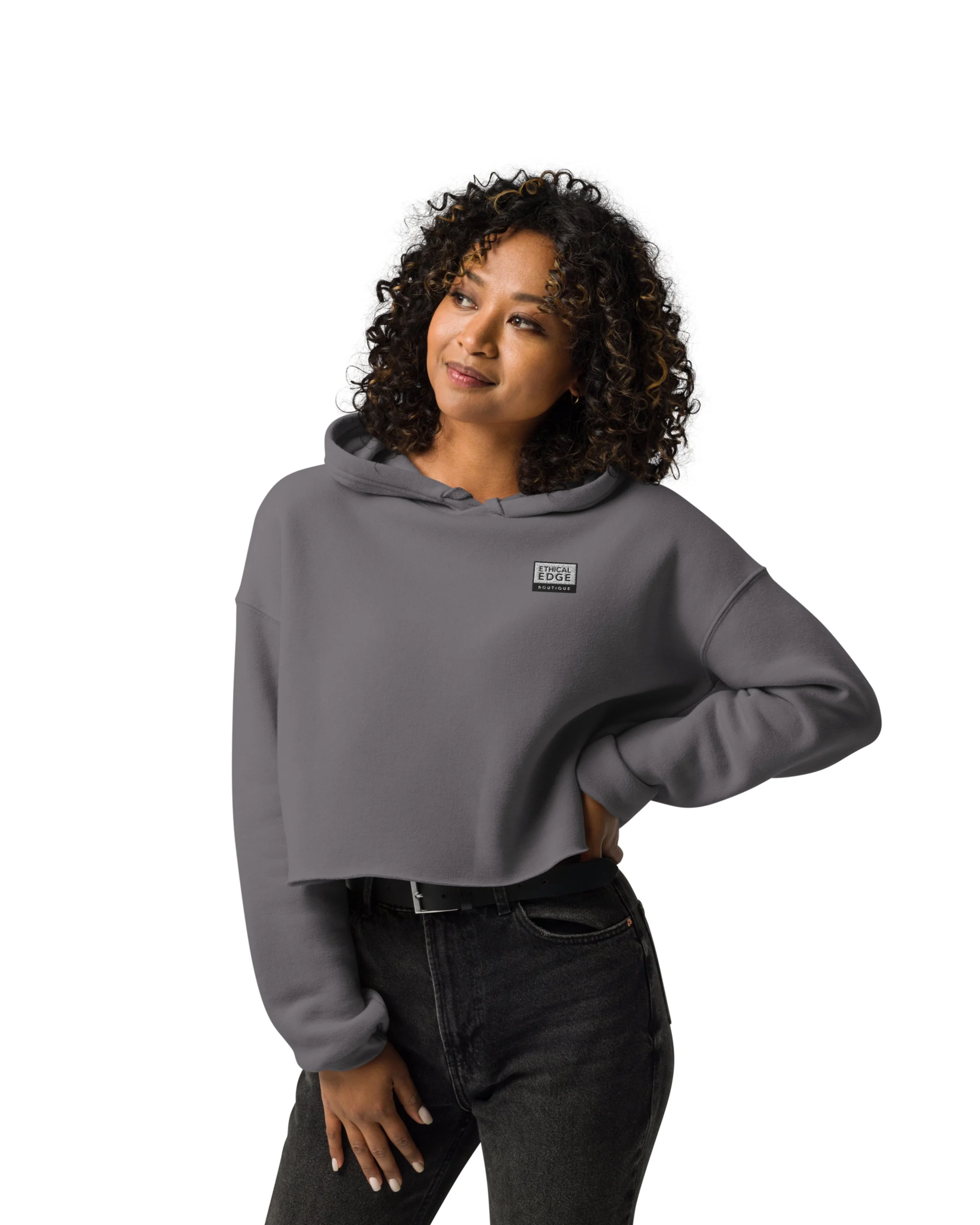 Young woman with curly hair wearing a gray hoodie and black jeans, posing against a white background.