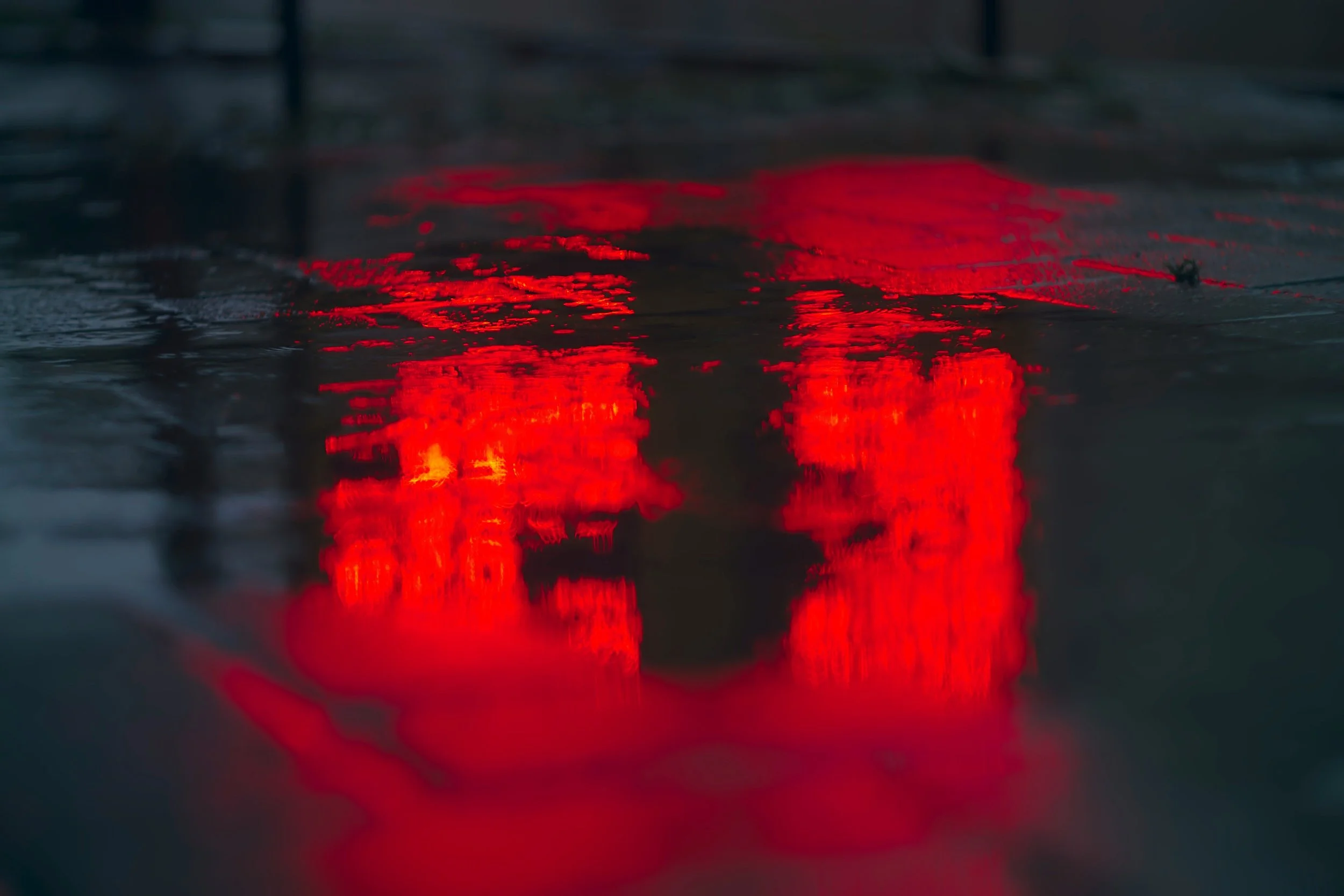 Red brake light reflections on a wet road surface at night.