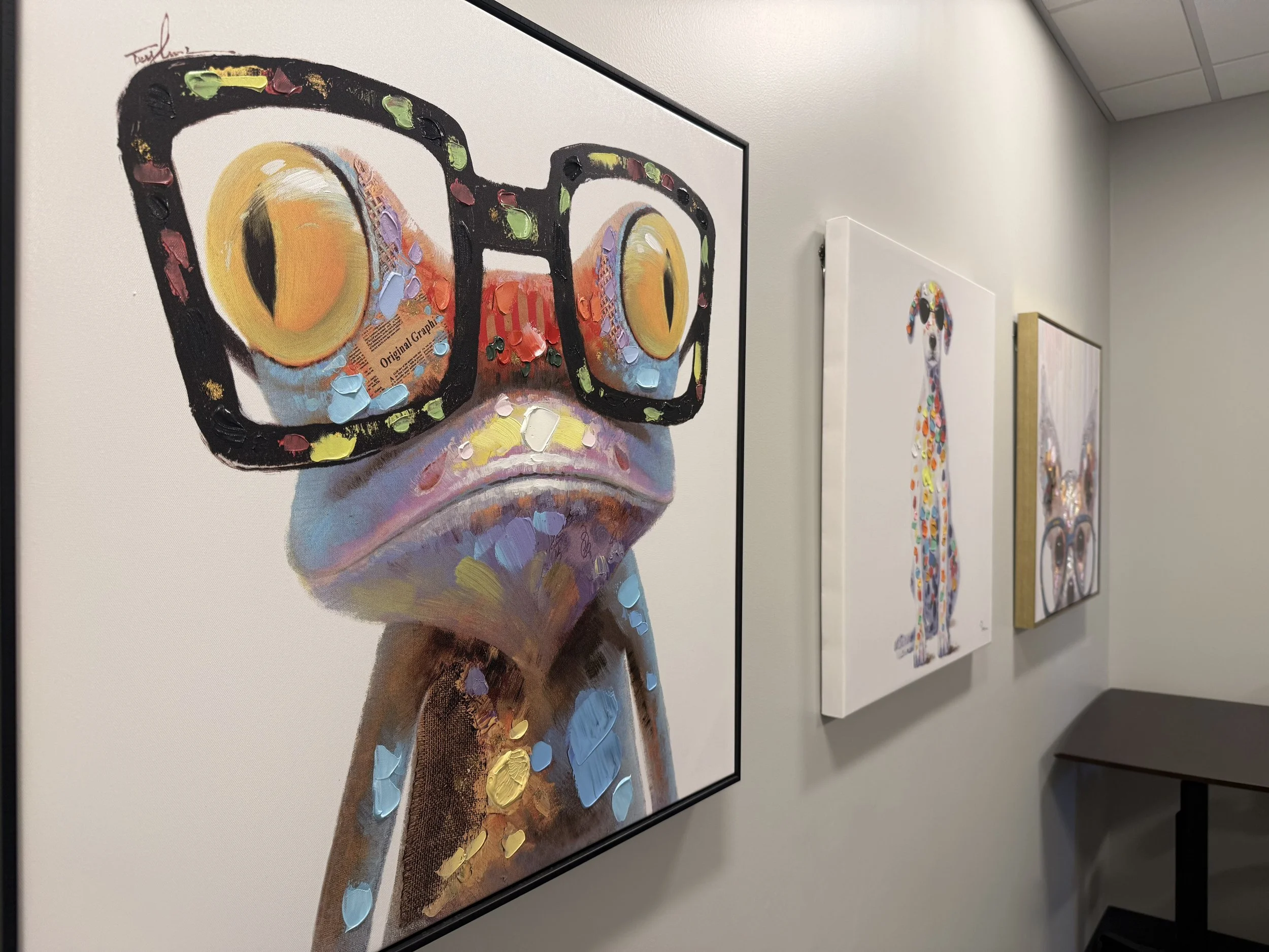 Colorful gallery wall featuring animal artwork, including a dog with glasses, a tall dog, and an animal with glasses, in a well-lit room.