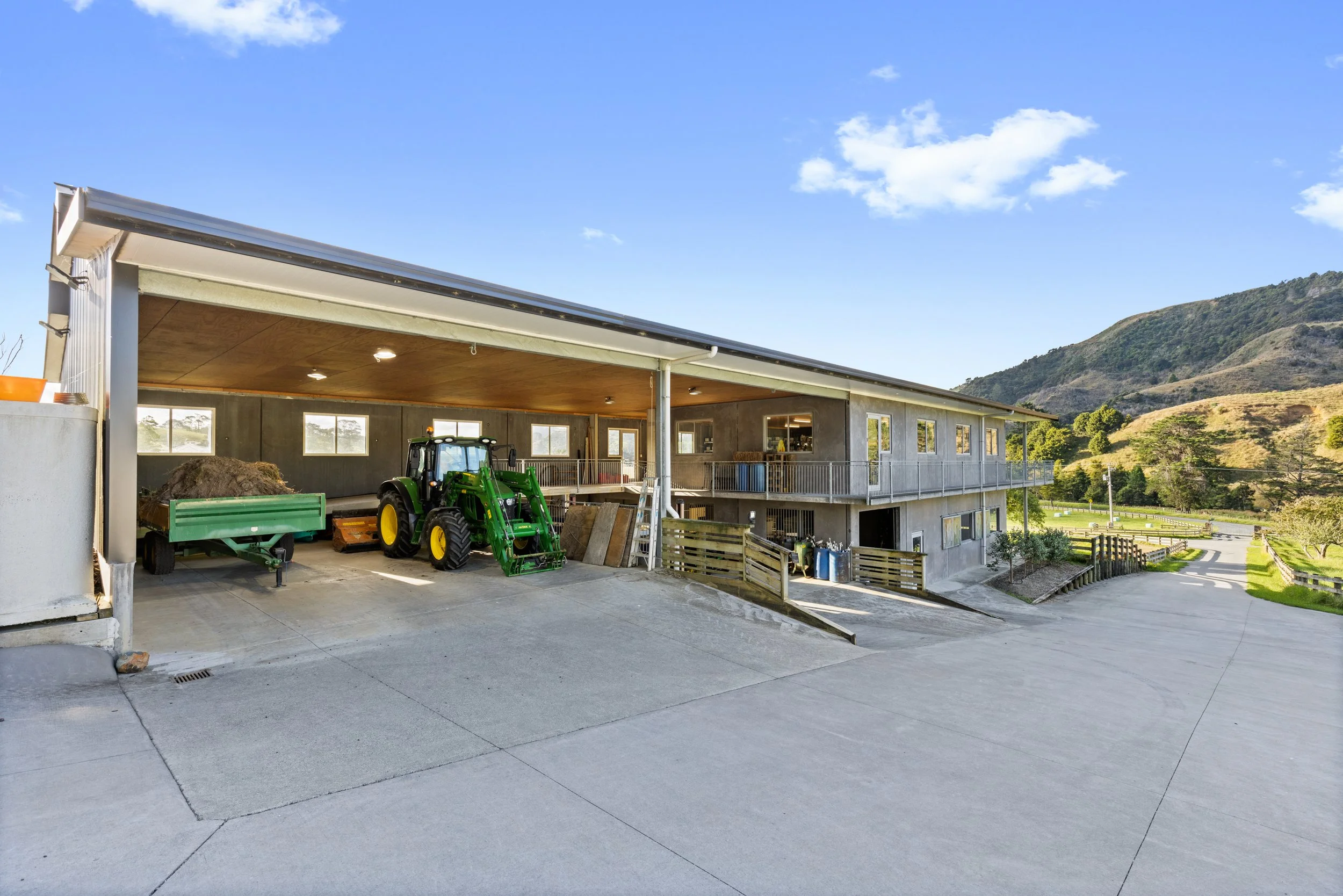 A building with a covered outdoor area, a tractor, and farming equipment in California countryside with rolling hills and trees in the background.