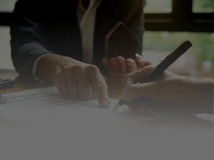 Persona en traje de negocios usando un teléfono móvil y una pluma para firmar documentos en una mesa