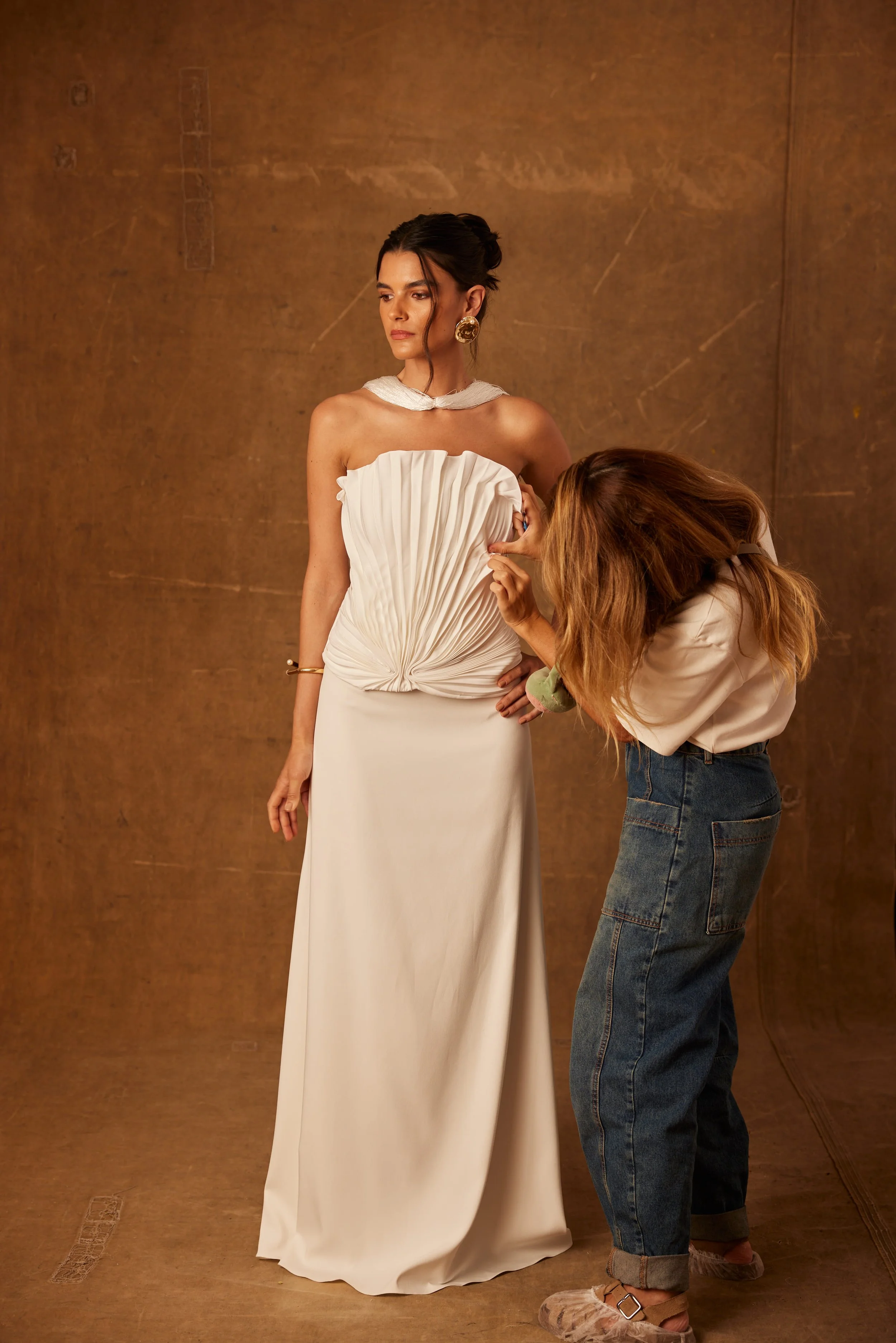 Mulher vestida com um vestido de noiva sendo ajustada por uma estilista em um estúdio de moda.