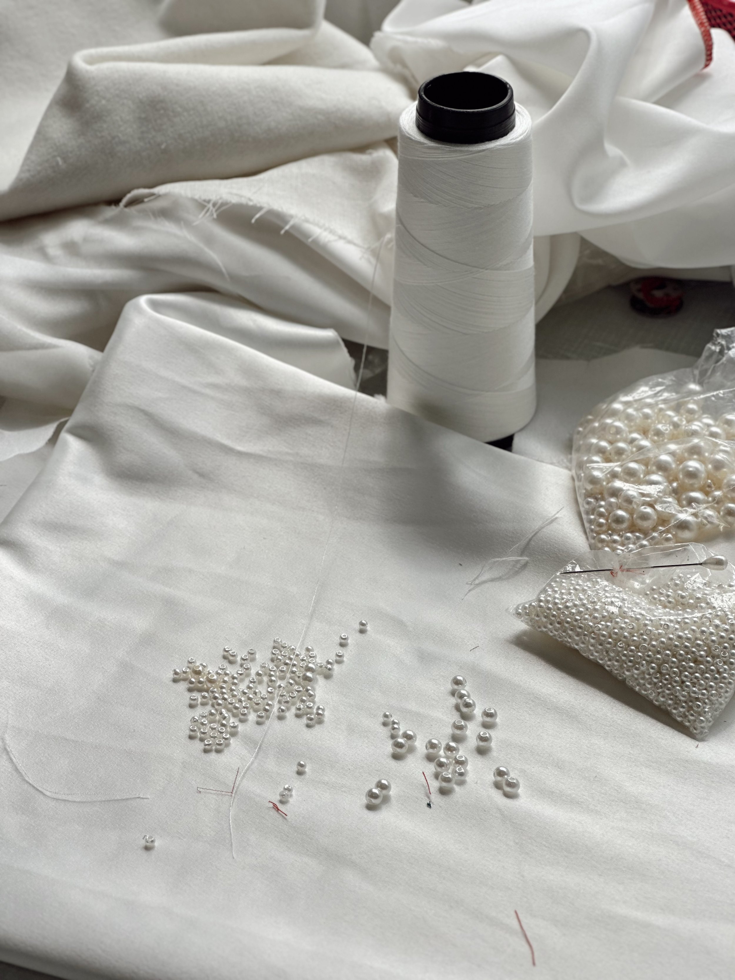 Fio de linha, pérolas brancas e tecidos brancos em uma mesa para artesanato ou costura.