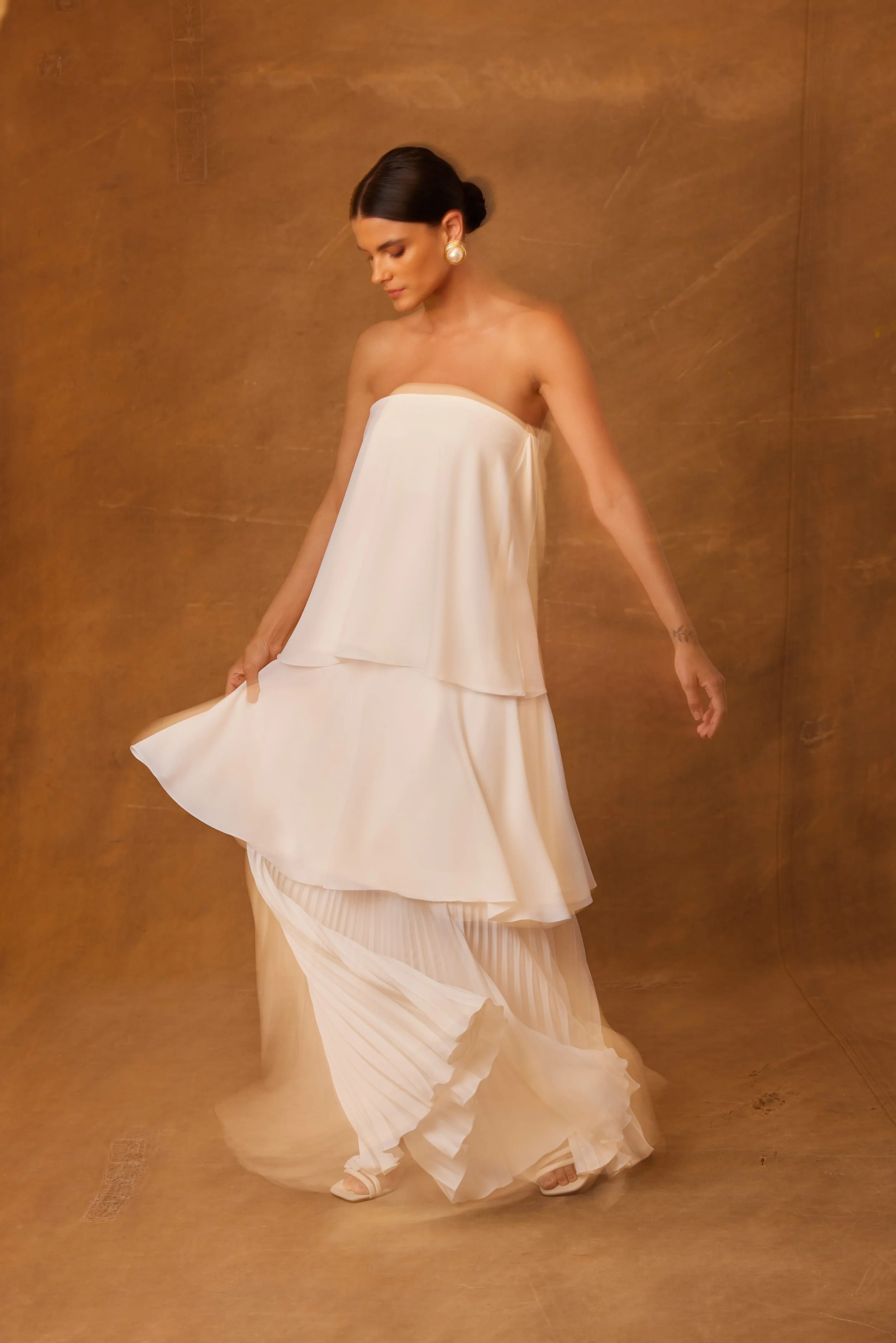 Mulher com vestido branco longo de tiras, com fundo cor de madeira.