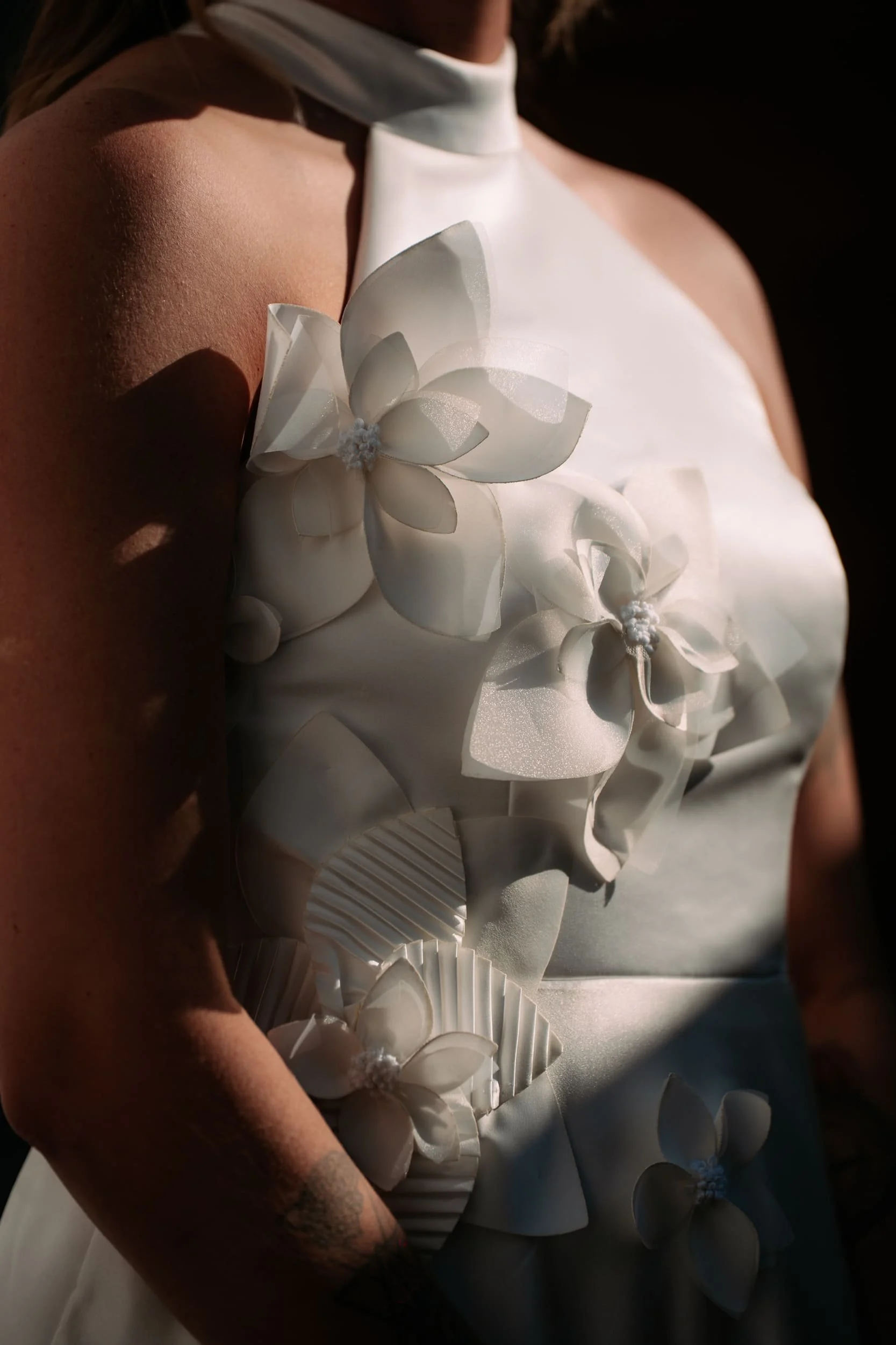 Detalhes de um vestido de casamento com flores de tecido branco e fitas, com pele visível do braço da mulher.