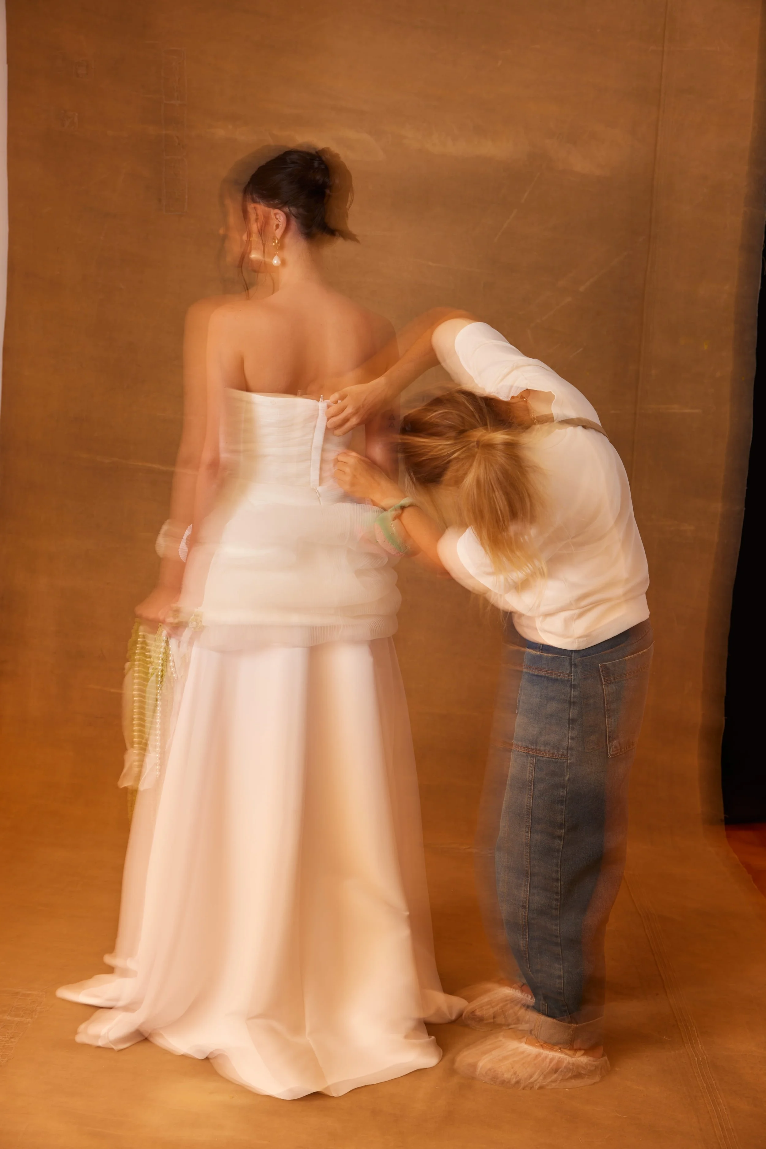 Pessoa ajustando o vestido de noiva enquanto a própria é ajudada por outra pessoa.