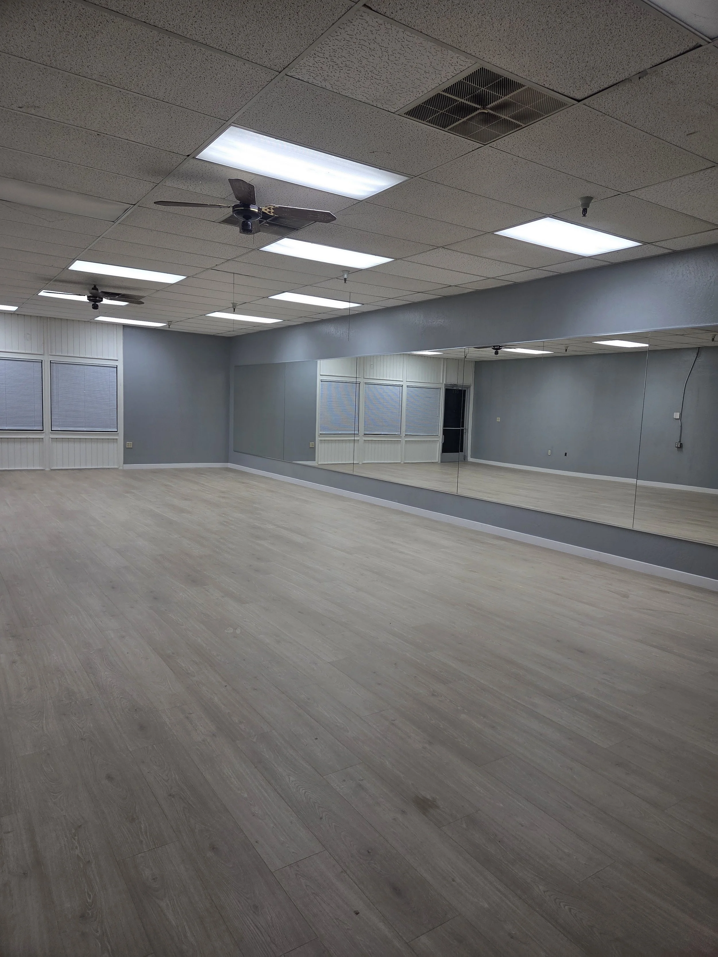 Bright dance studio with gray walls, light flooring, and a long wall of full length mirrors