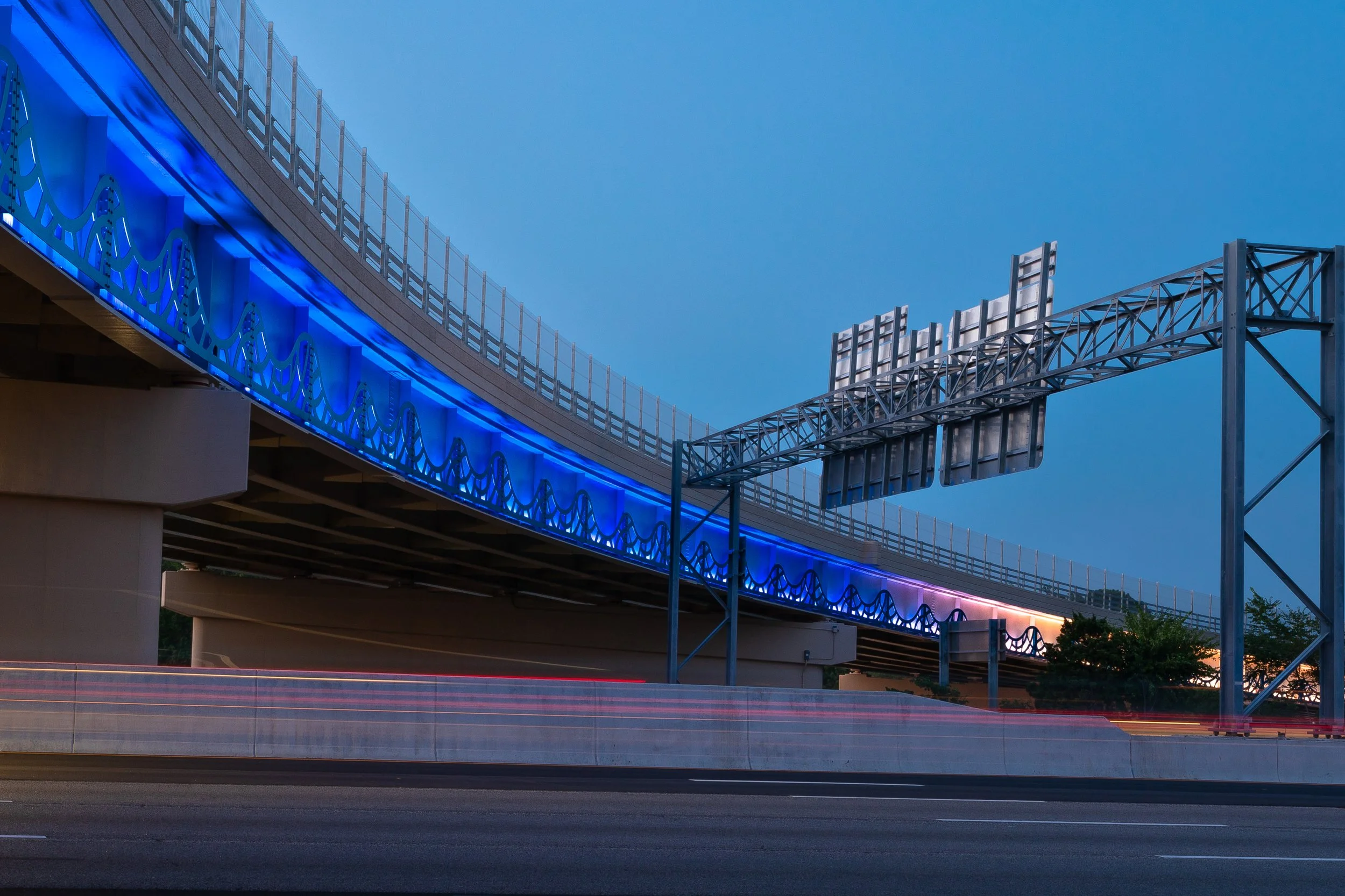A long exposure of a newly completed highway overpass in Virginia Beach. The bridge is decorated with a metal wave design that lights up in a gradient from blue to orange.