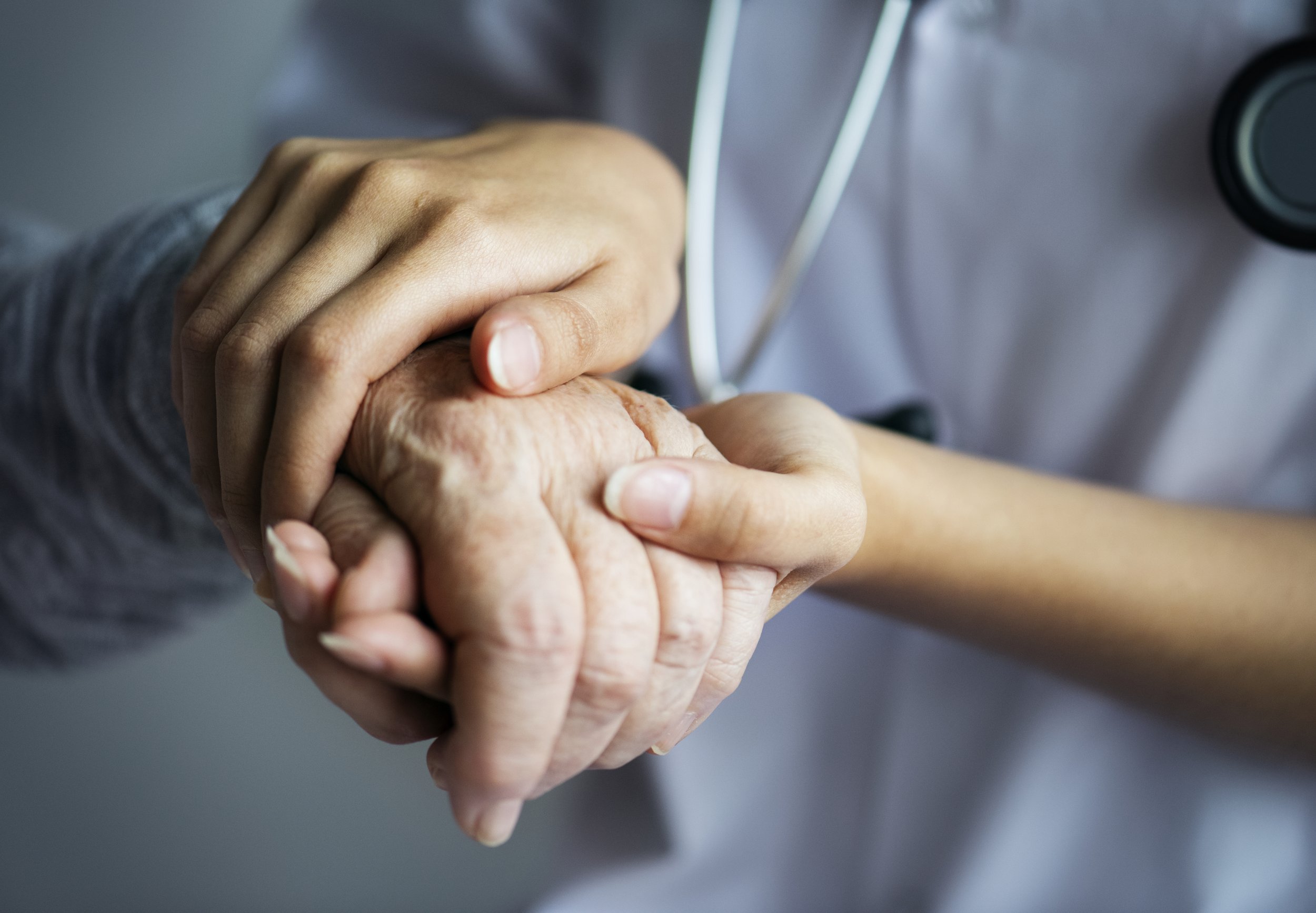 A healthcare professional holding an elderly patient's hand.