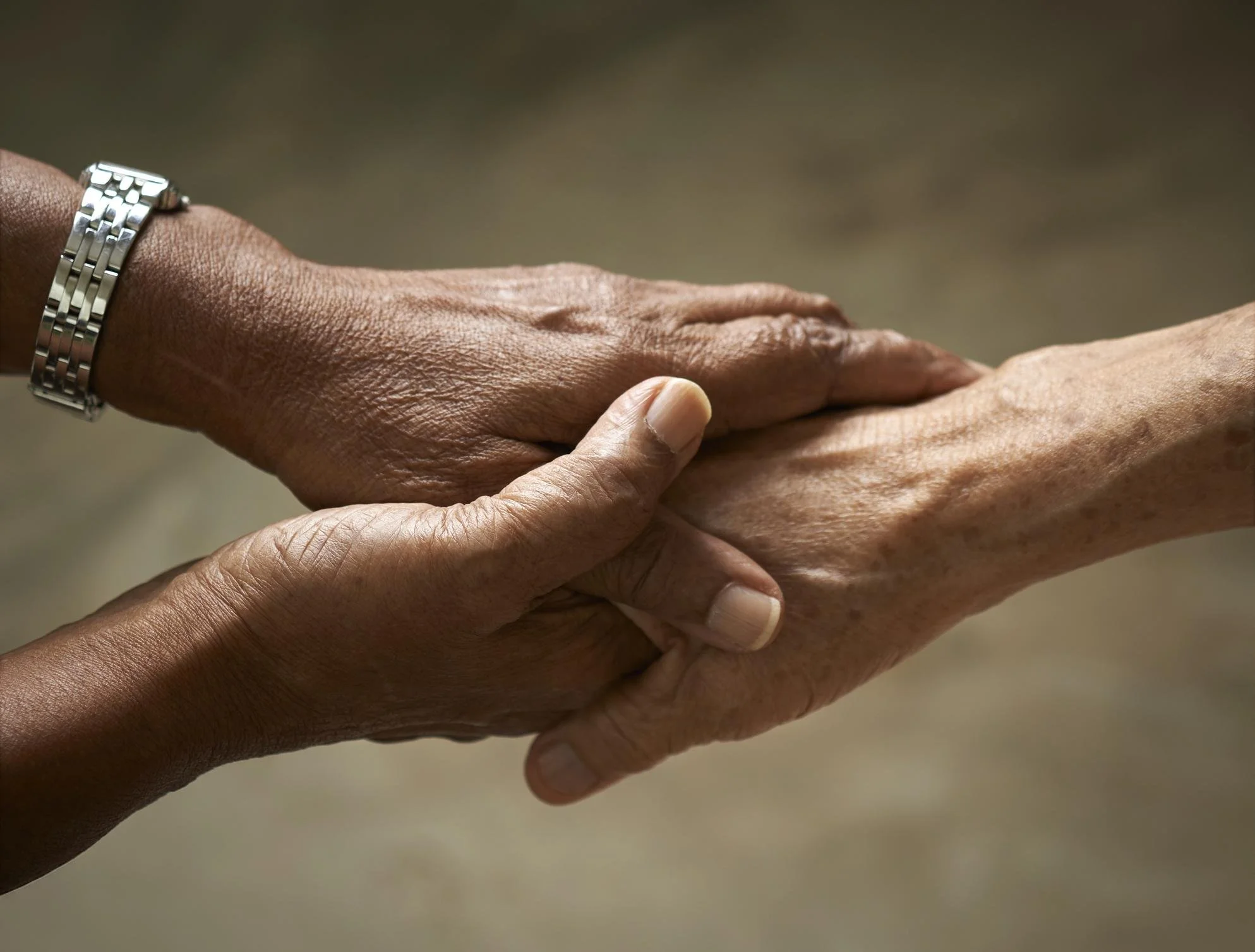 Two hands, one darker-skinned and one lighter-skinned, holding each other's wrists in a gentle, supportive manner.