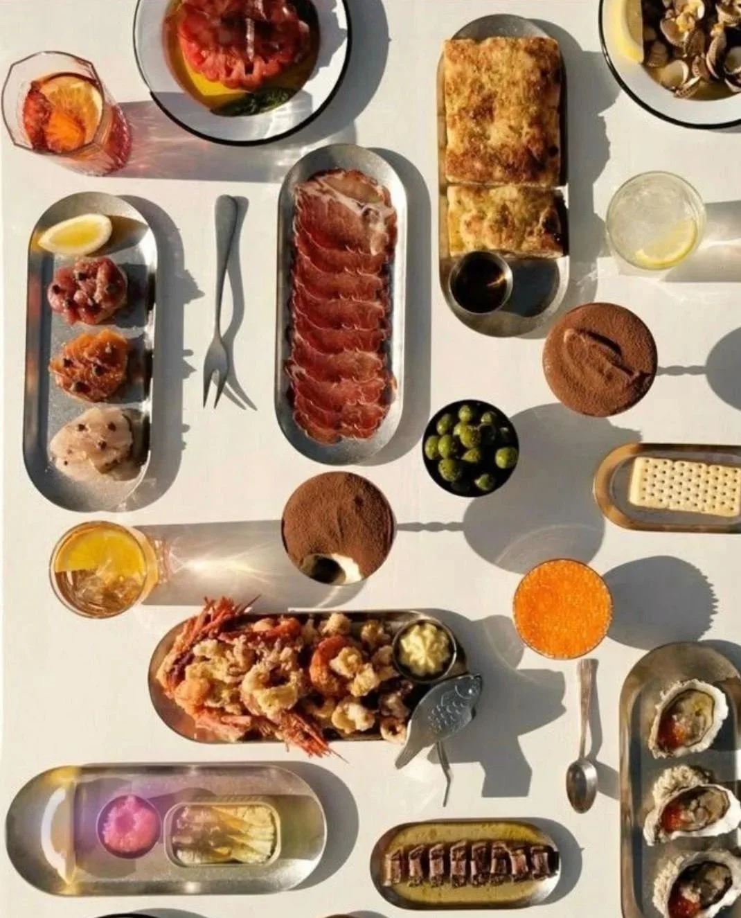A variety of dishes including sashimi, seafood, bread, desserts, and drinks on a white table.