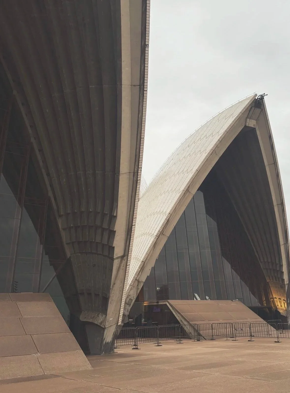 Close-up view of the Sydney Opera House, showcasing its distinctive sail-like white shells and modern architectural design against a gray sky.