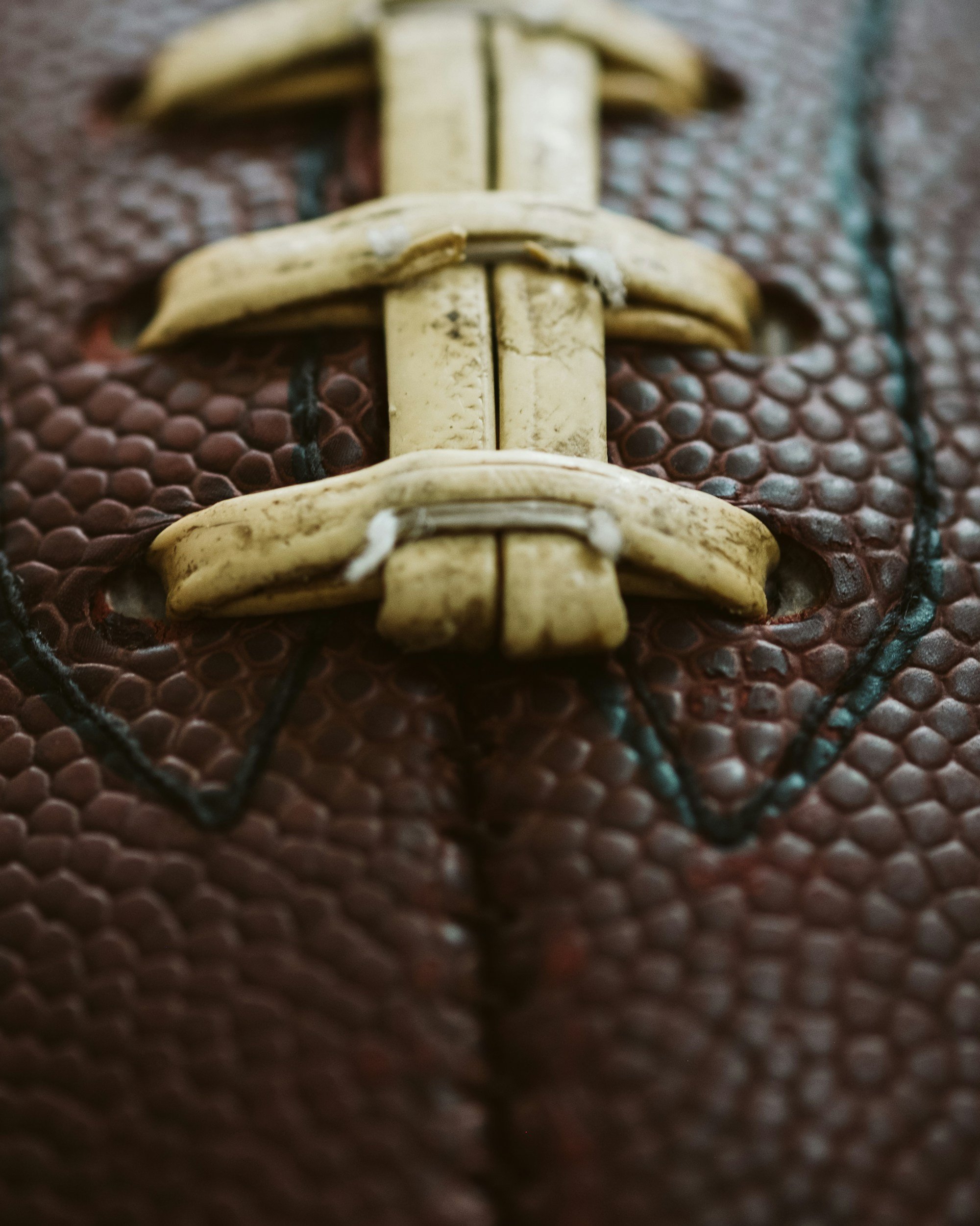 Close-up of a football lacing, showing cream-colored laces on a textured brown football with black stitching.