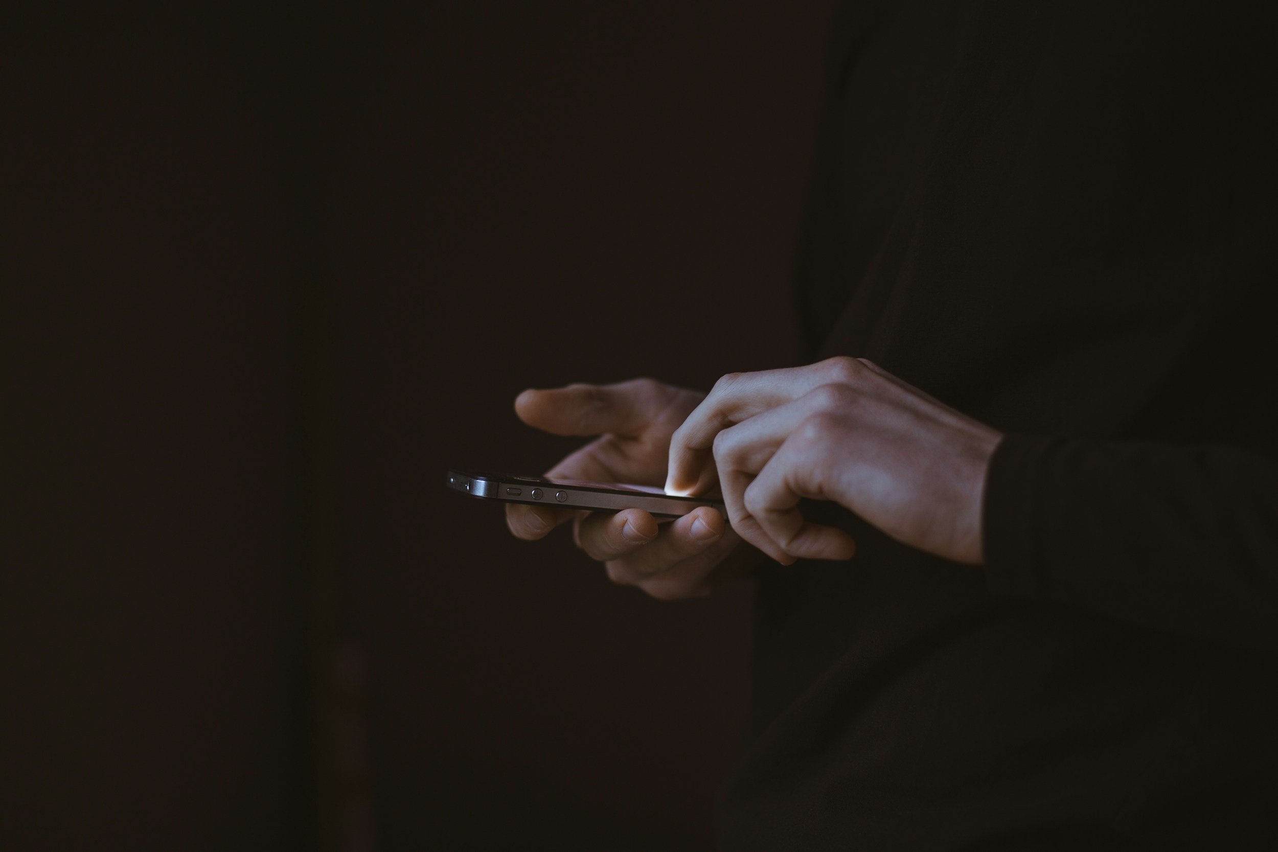 Person holding and using a smartphone in a dark environment.