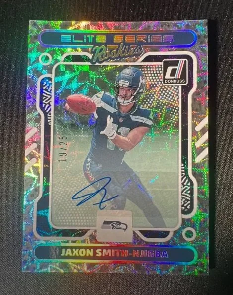 Holographic football trading card of Jaxon Smith-Njigba from Donruss Elite Series Rookie set, featuring a player in a Seahawks uniform holding a football, with an autograph and holographic effects.