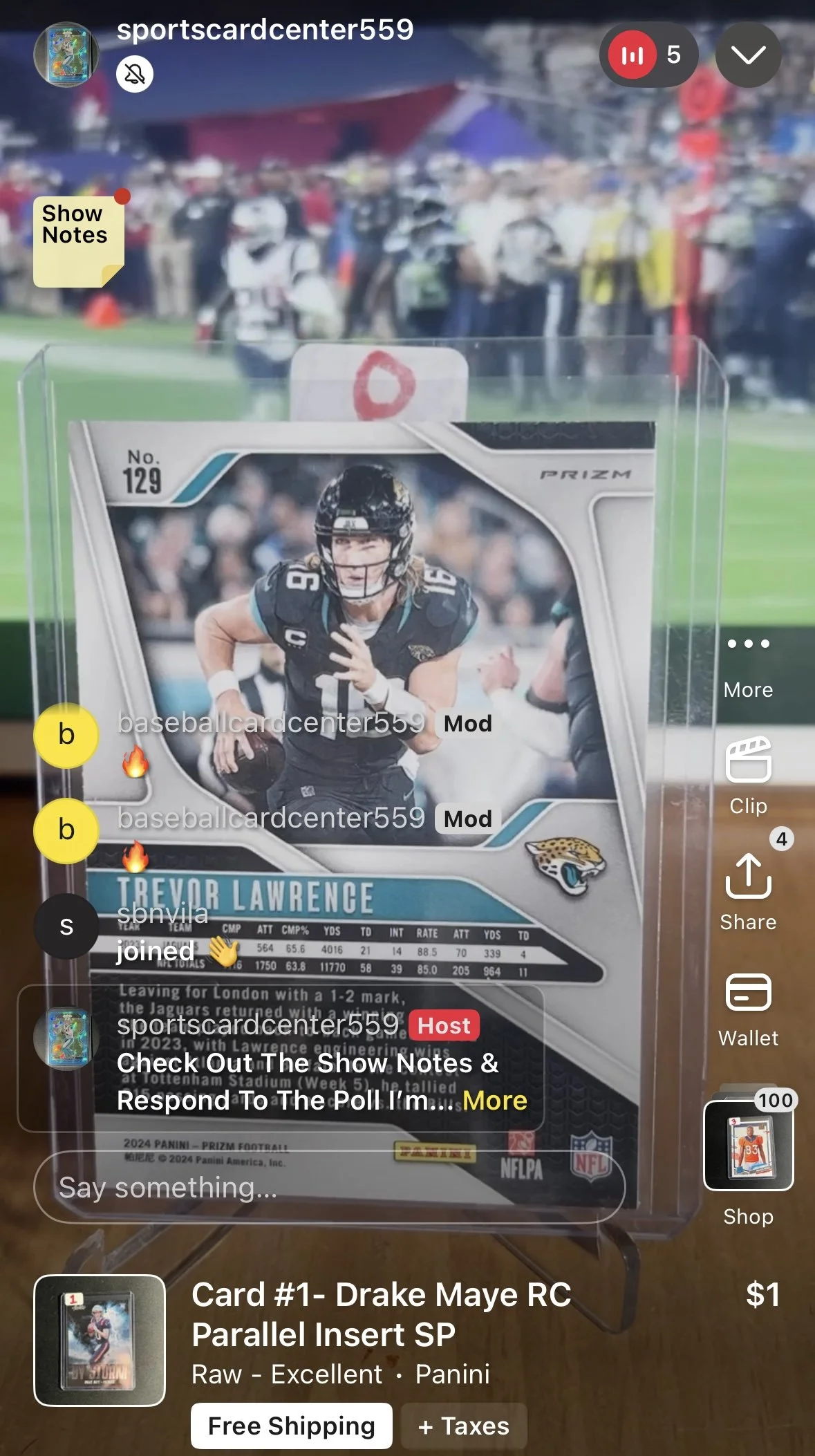 A football trading card of Trevor Lawrence from the Jacksonville Jaguars is displayed inside a clear protective case, with a crowd of people in the background at a sports event.
