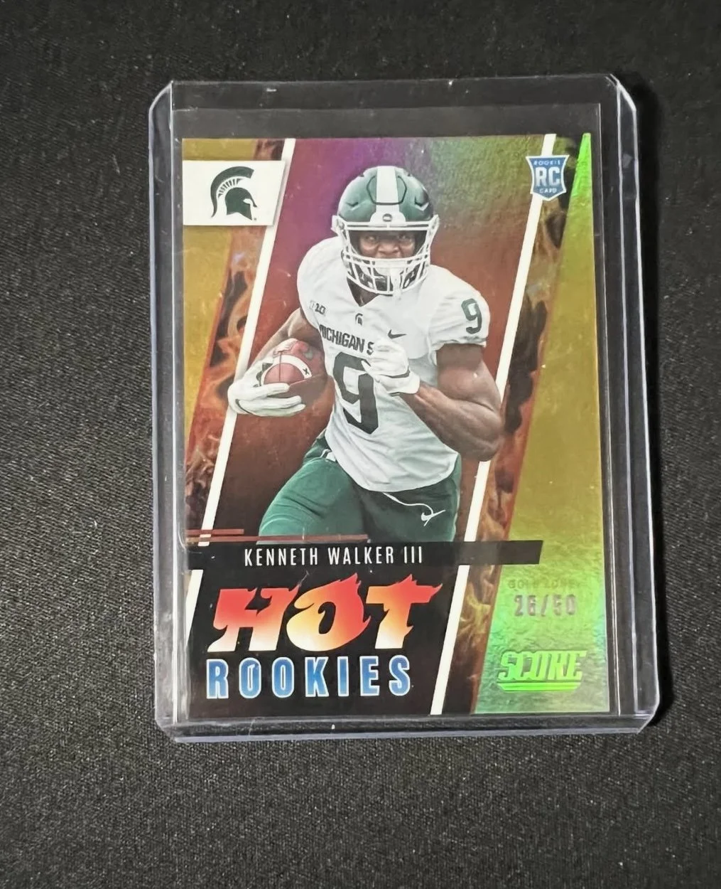 A collectible sports card featuring Kenneth Walker III, a football player for Michigan State, in a white uniform with green numbers, holding a football, with the text 'Hot Rookies' and '26/50' on a holographic background.