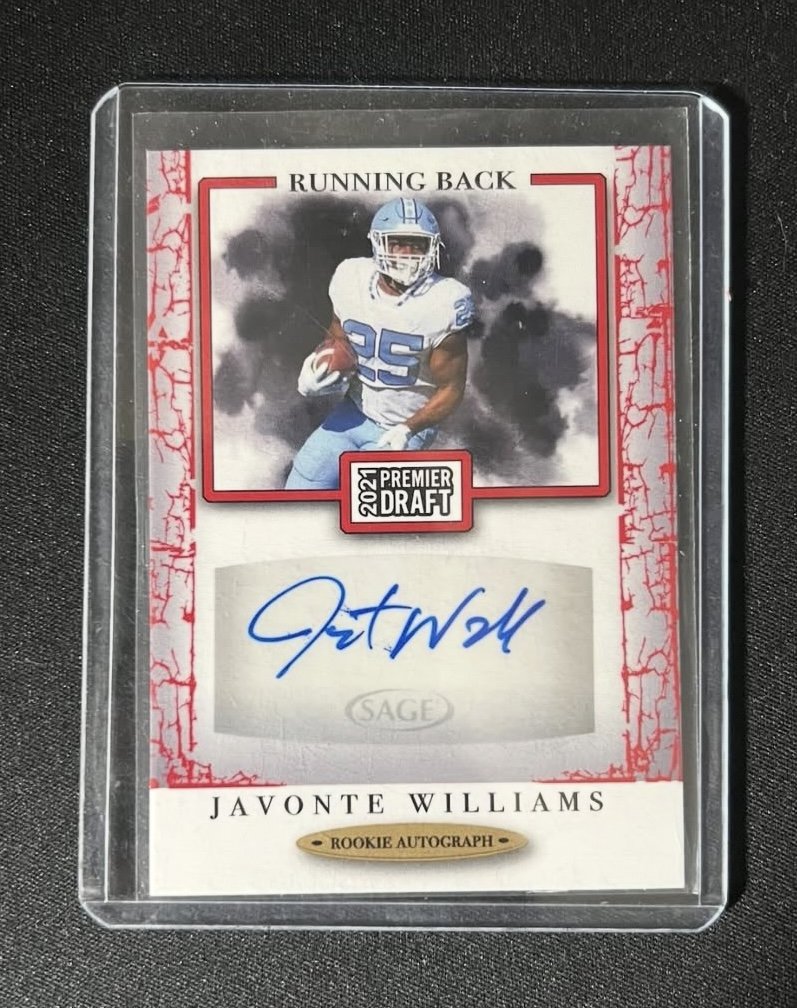 Javonte Williams rookie football autograph card with an image of Williams in a white and blue jersey running with a football, signed in blue ink, with black smoke or clouds in the background.