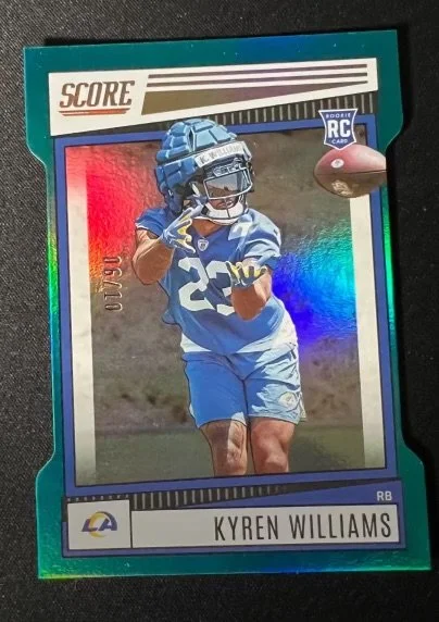 Football trading card of Kyren Williams in a blue uniform holding a football, with a holographic border and rodent RC badge, on a black background.