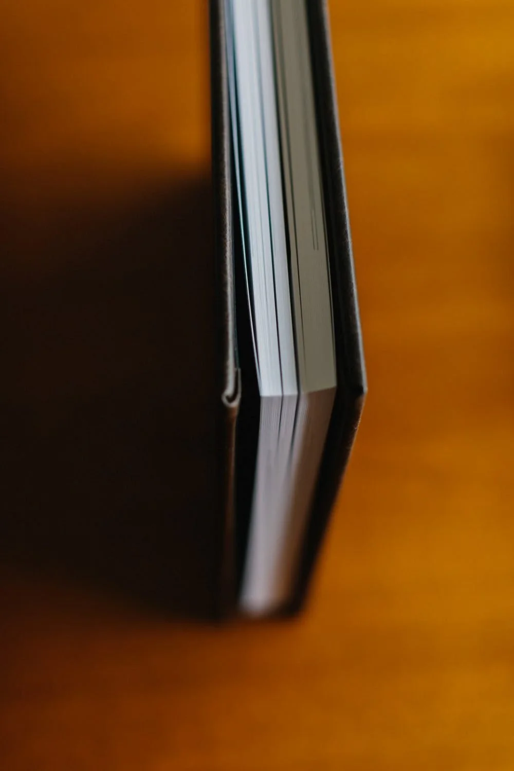 Close-up of a book or notebook with a brown cover, viewed from the side, resting on a wooden surface.