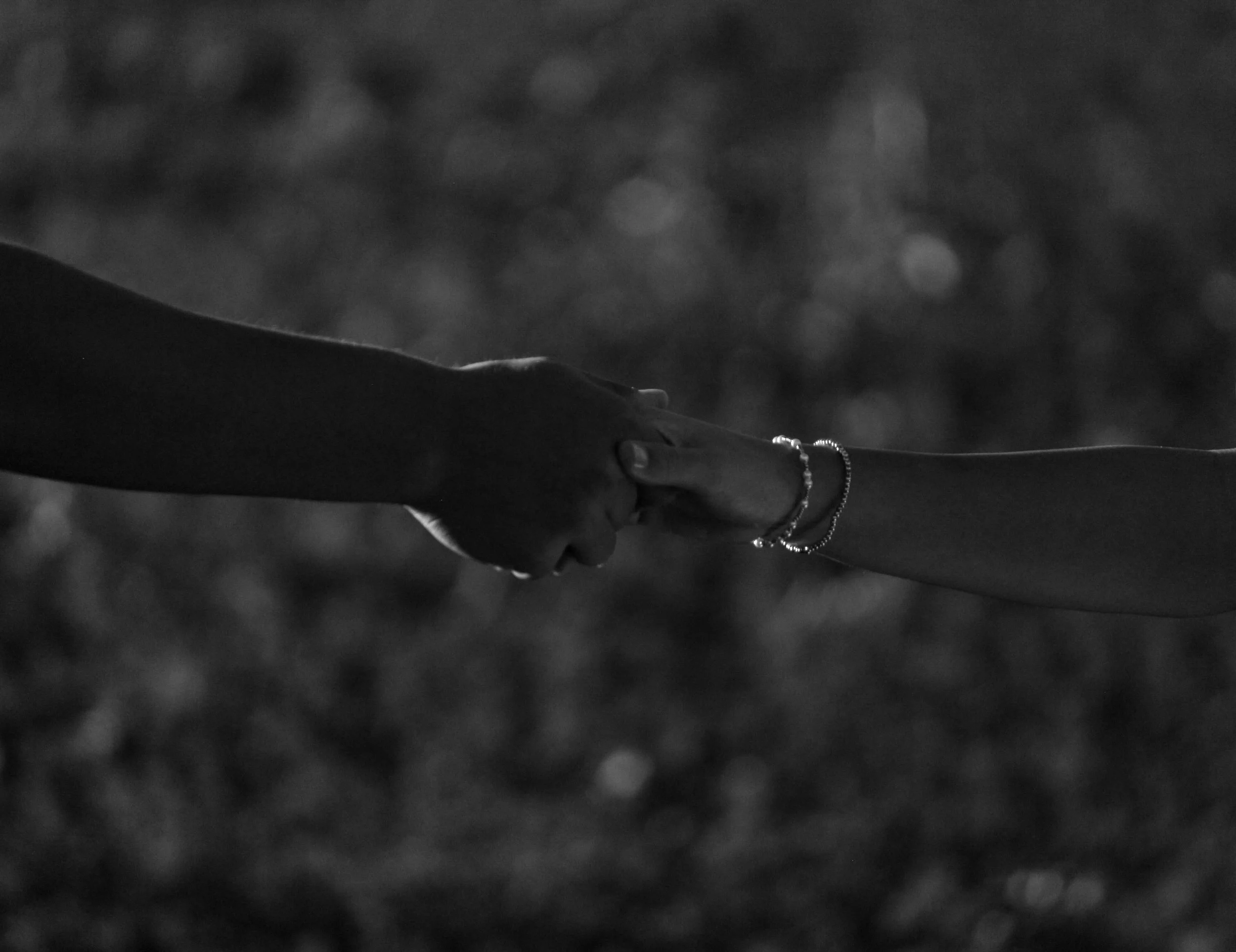 Two people holding hands with interlocked fingers, wearing bracelets, in a black and white photograph.