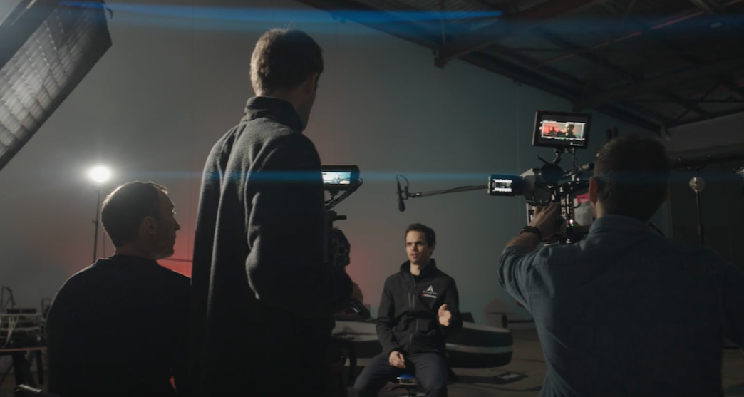 A professional Watchpost film crew on a dark set, using cinema cameras and monitors to capture a seated interview.