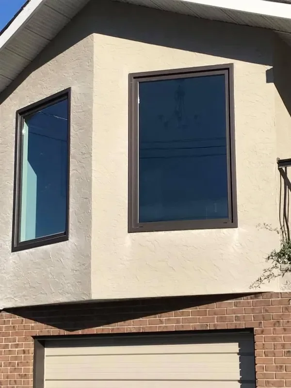 Close-up of a modern building's exterior showing two large, rectangular windows and a brick garage door below.