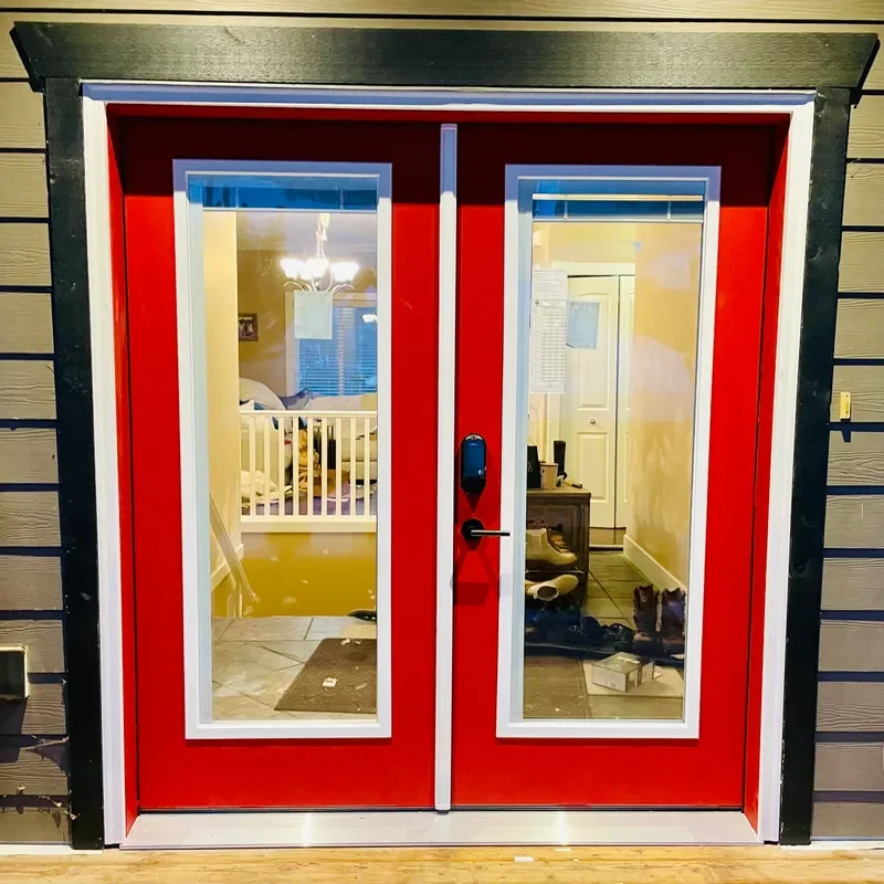 Red double front doors with glass panels, a keypad lock, and view of the interior including a crib and a hallway with shoes.